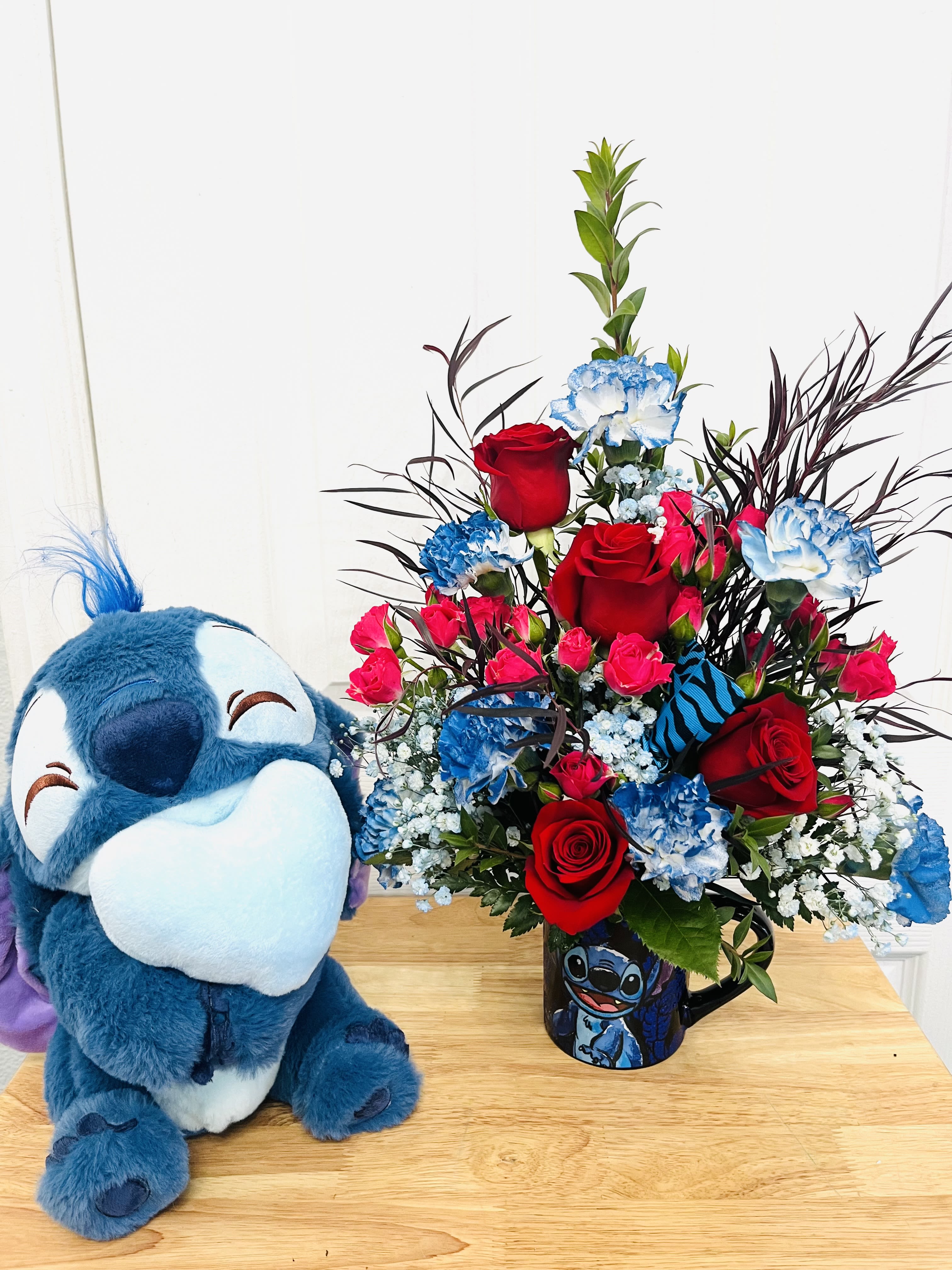 Bouquet of red roses and blue carnations in a Stitch mug beside a plush Stitch toy