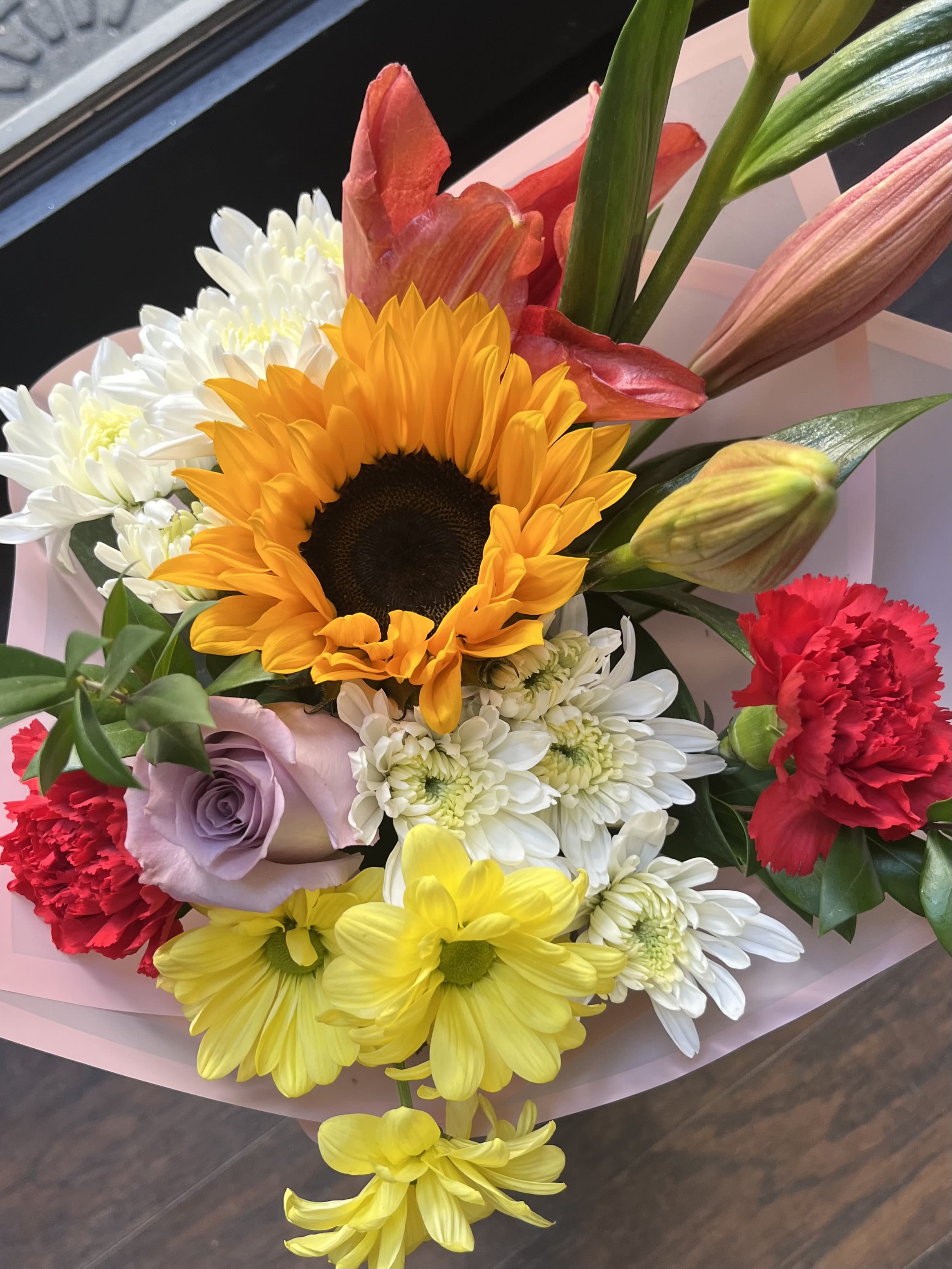 Bright mixed bouquet with sunflower, lilies, carnations, roses and daisies wrapped in pink paper