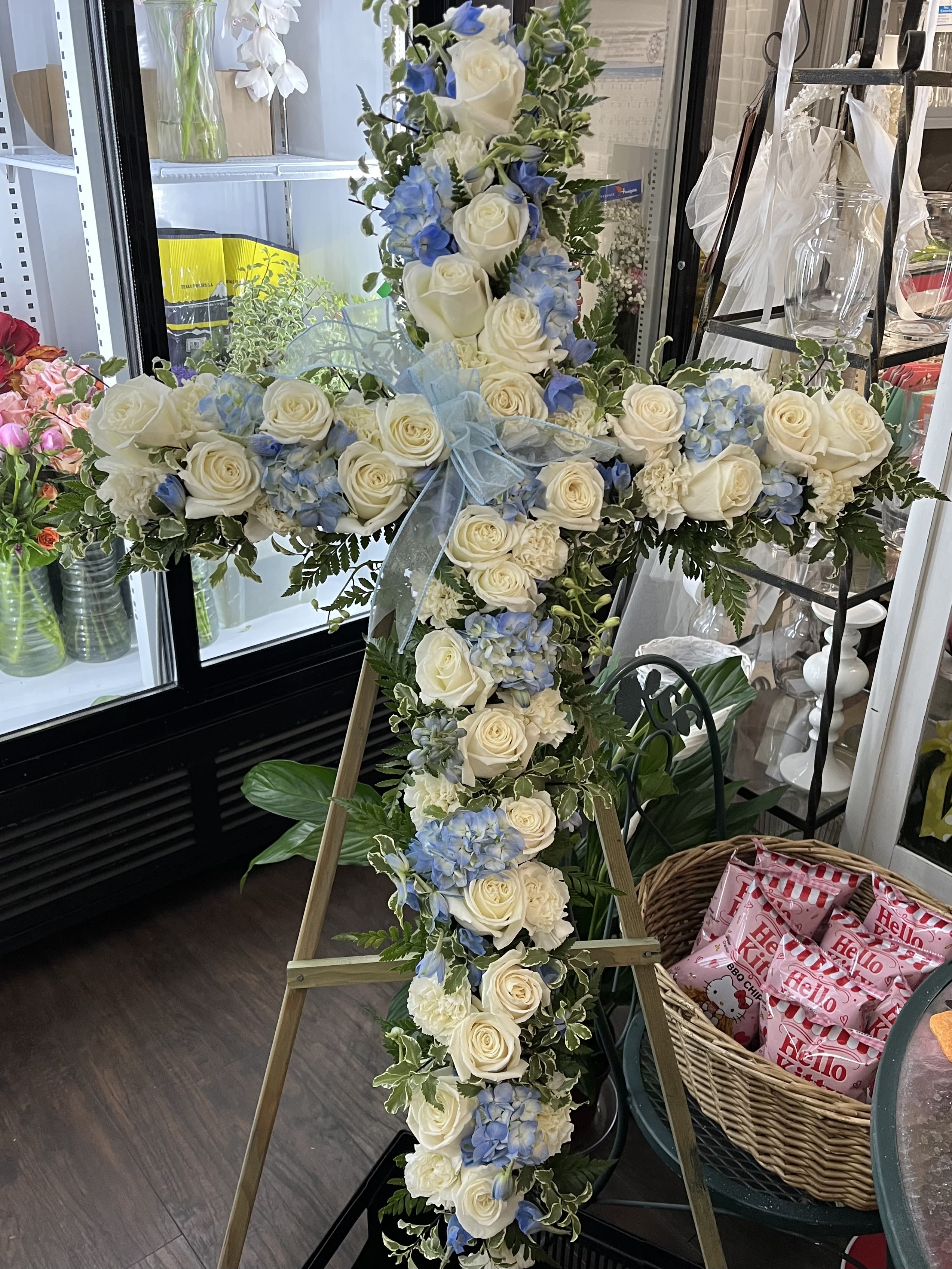 Cross-shaped floral tribute with white roses and blue hydrangeas on an easel