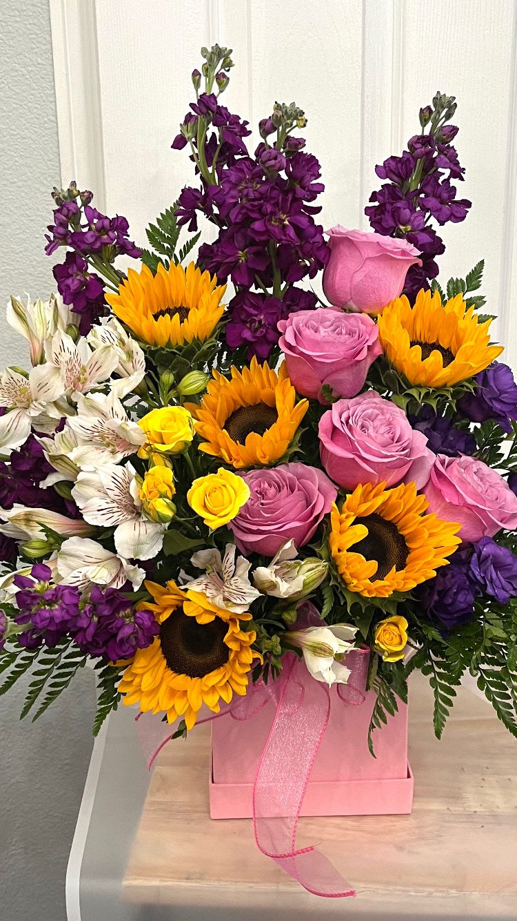 Pink roses, sunflowers, and purple flowers arranged in a pink box
