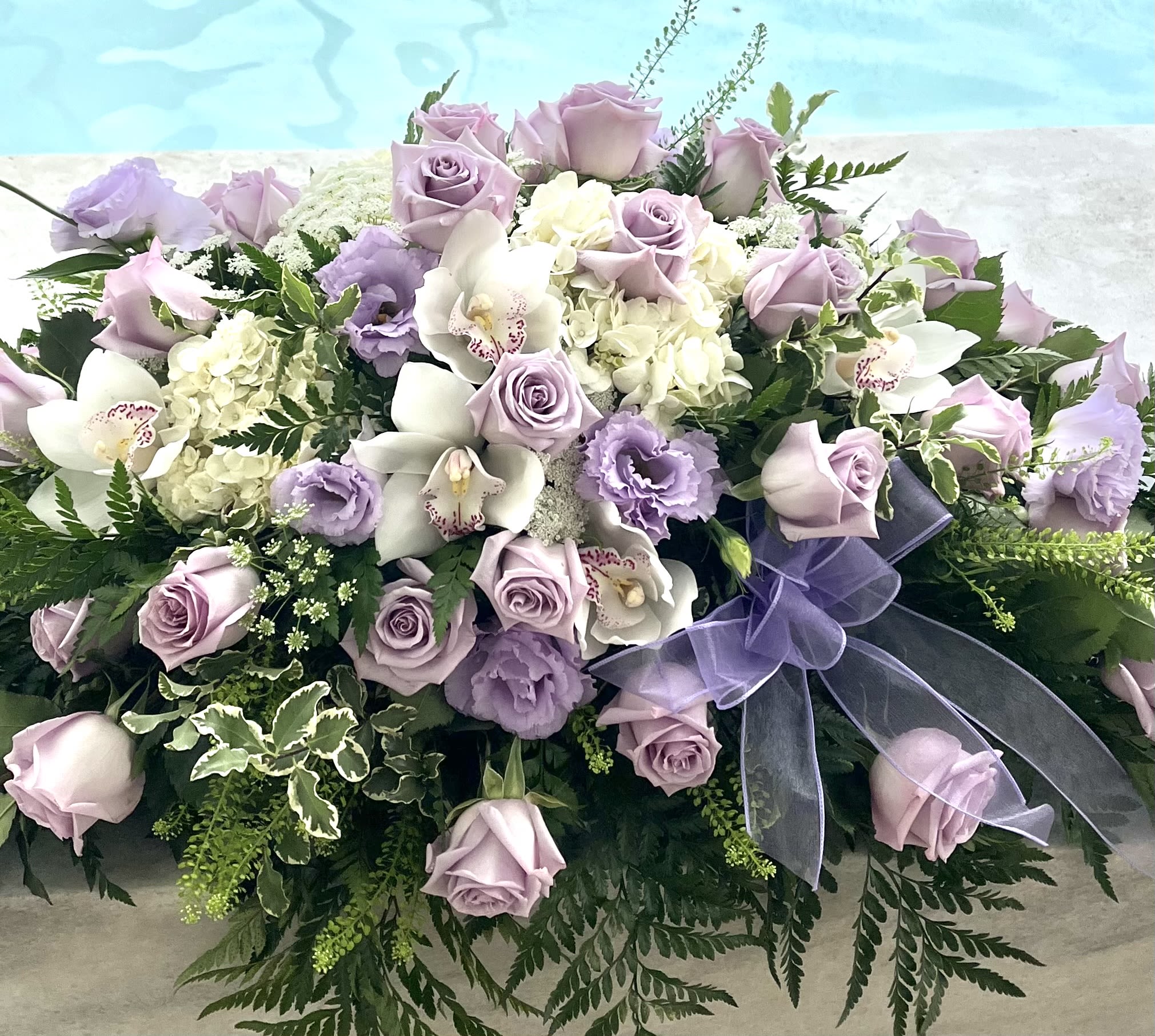 Lavender roses and white orchids arranged with a purple ribbon.