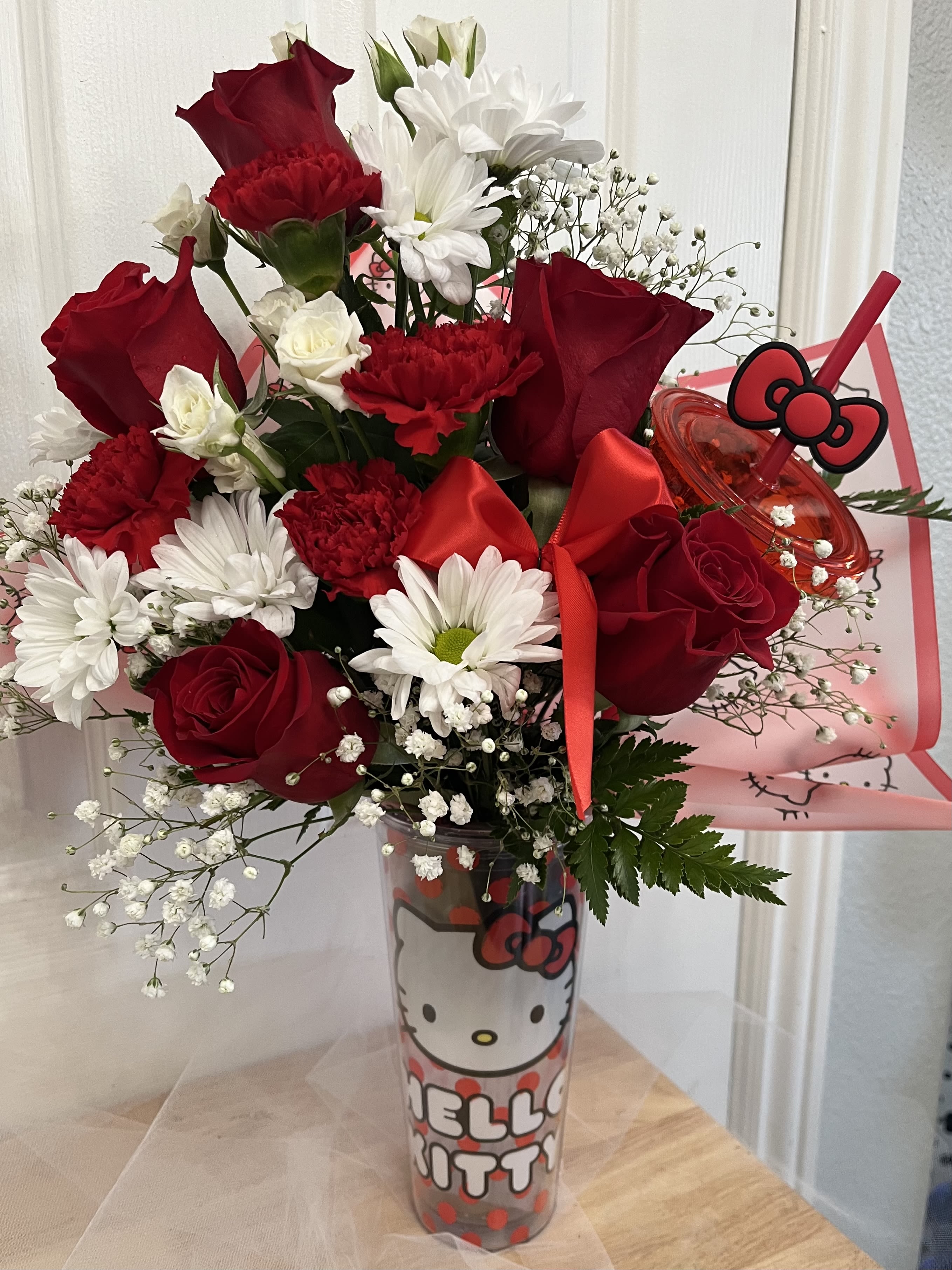 Red roses and white daisies in a Hello Kitty tumbler with a red bow.