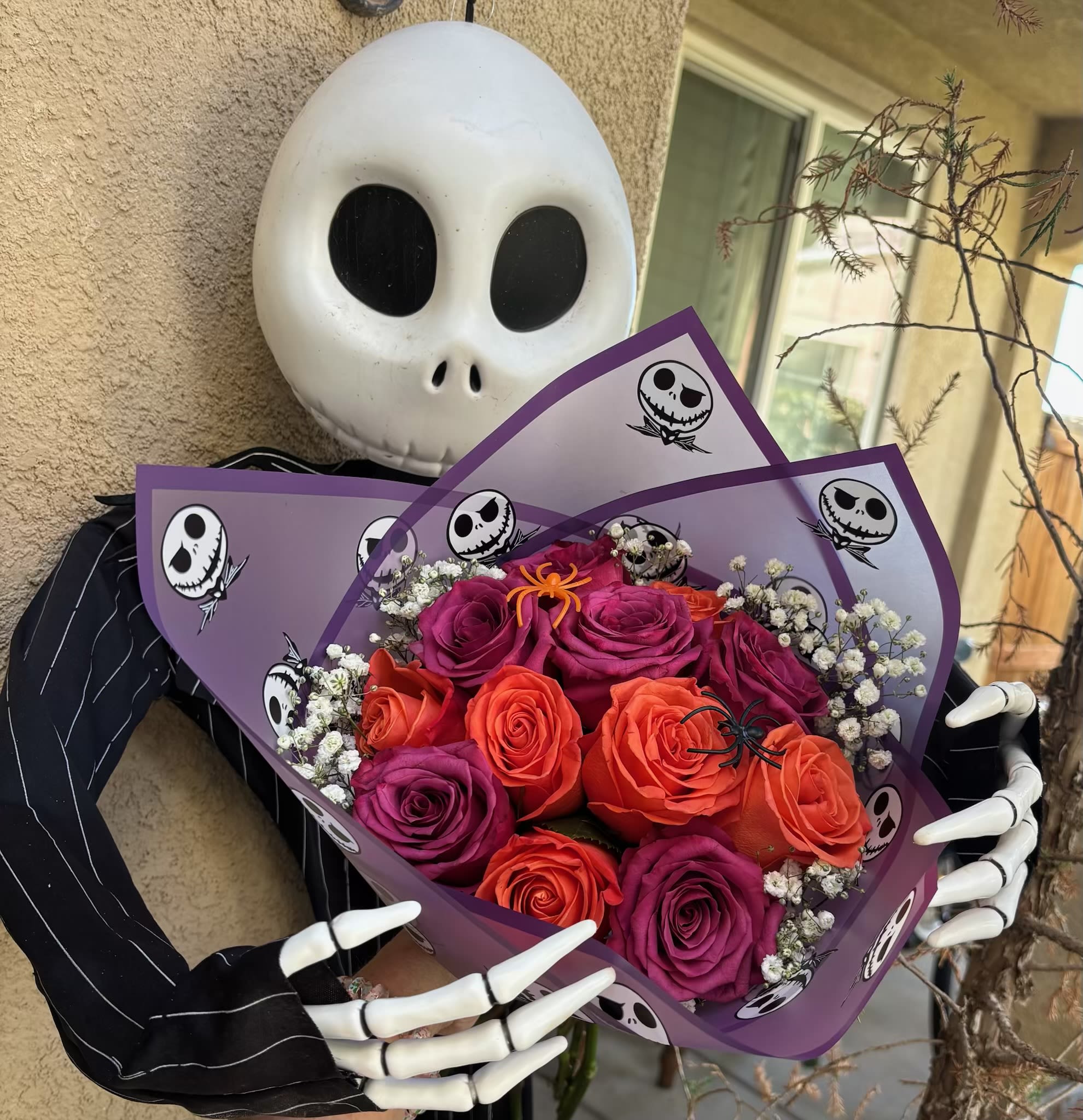 Bouquet of orange and purple roses wrapped in purple paper with skull prints