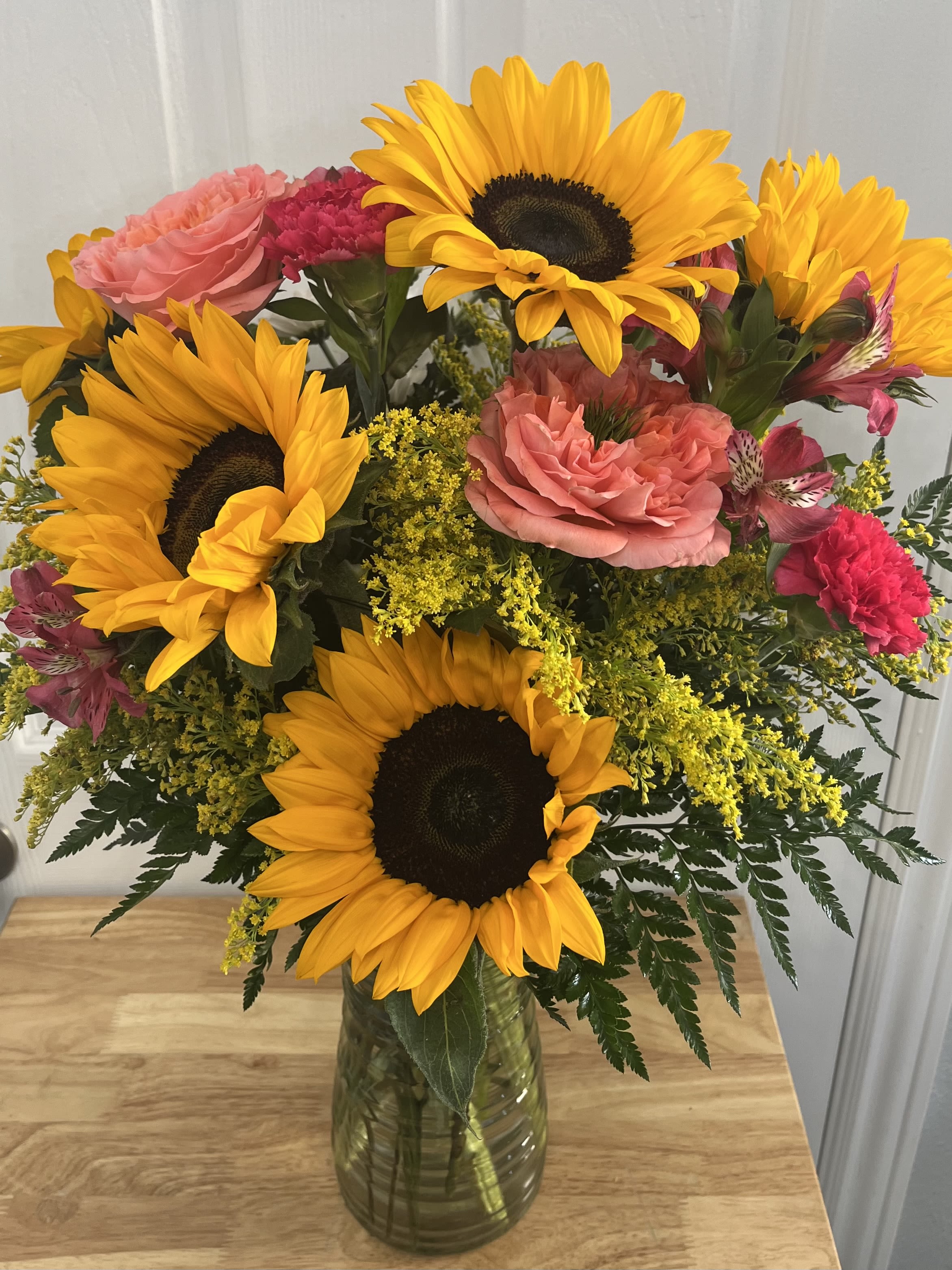 Bouquet of sunflowers, pink roses, and carnations in a glass vase