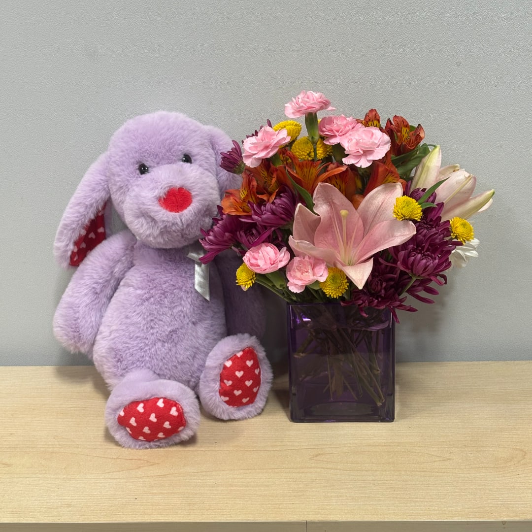 Purple plush bunny beside a mixed flower arrangement in a vase