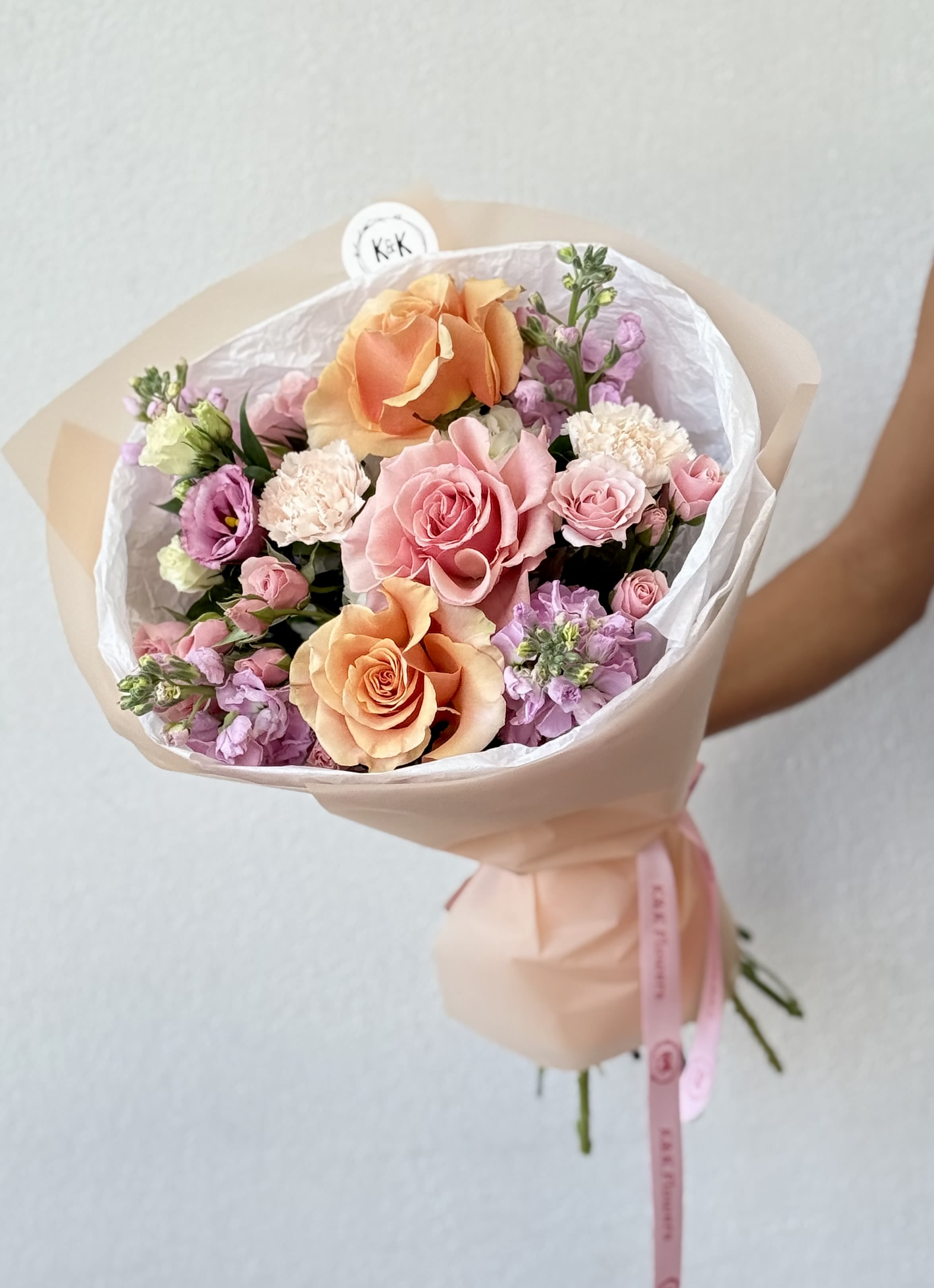 Bouquet of peach and pink roses with lavender blooms wrapped in pale paper