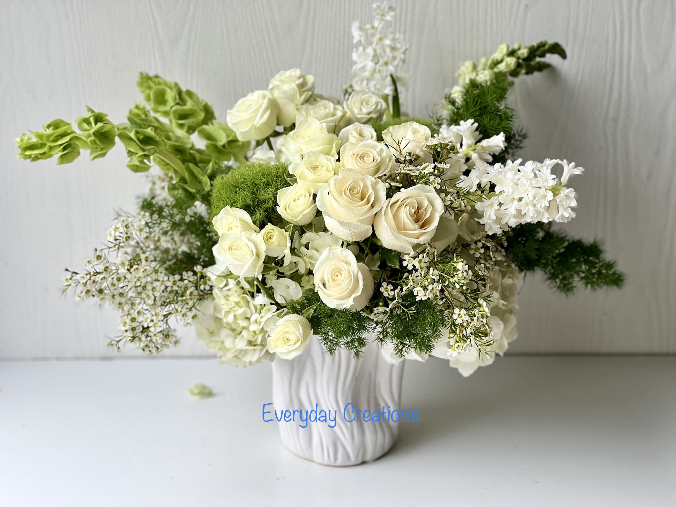 EC84 - Morninig Stars - The  Morning Stars floral arrangement is a brilliant expression of peace and soft serenity. White roses, snapdragon, hydrangea, white wax flower and hyacinth, and Oriental lilie are accented with the bright green stems of Bells of Ireland and a gorgeous assortment of lush greens to create a harmonious and balanced color palette. This all-white and green flower arrangement is idea for any occasion from birthdays and anniversaries, to congratulating someone on a new job or offering heartfelt sympathy. It's a versatile floral arrangement that looks equally beautiful in a modern or traditional setting. 