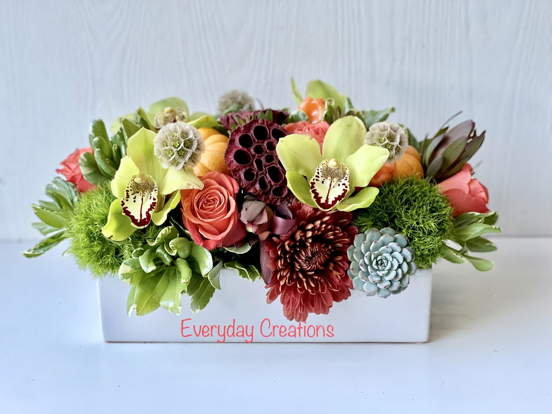 Thanksgiving Centerpiece EC103 - Celebrate the beauty of autumn with our expertly crafted long and low Thanksgiving centerpiece, perfect for any table or holiday gathering. This eye-catching floral arrangement features vibrant orange roses, lush green cymbidiums, unique succulents, textured green ball flowers, warm safflower, and soft Cremon blooms. Each flower is thoughtfully arranged by our skilled florists in a chic white ceramic container, creating a centerpiece that exudes elegance and seasonal charm. Whether you're hosting a family dinner or simply enhancing your fall home decor, this centerpiece brings warmth, beauty, and a touch of sophistication to your space. Perfect for Thanksgiving, autumn weddings, or as a thoughtful gift. Order your Thanksgiving centerpiece today and let the rich colors and textures of fall transform your table into a festive masterpiece. mesurement: 12"X 5.5"