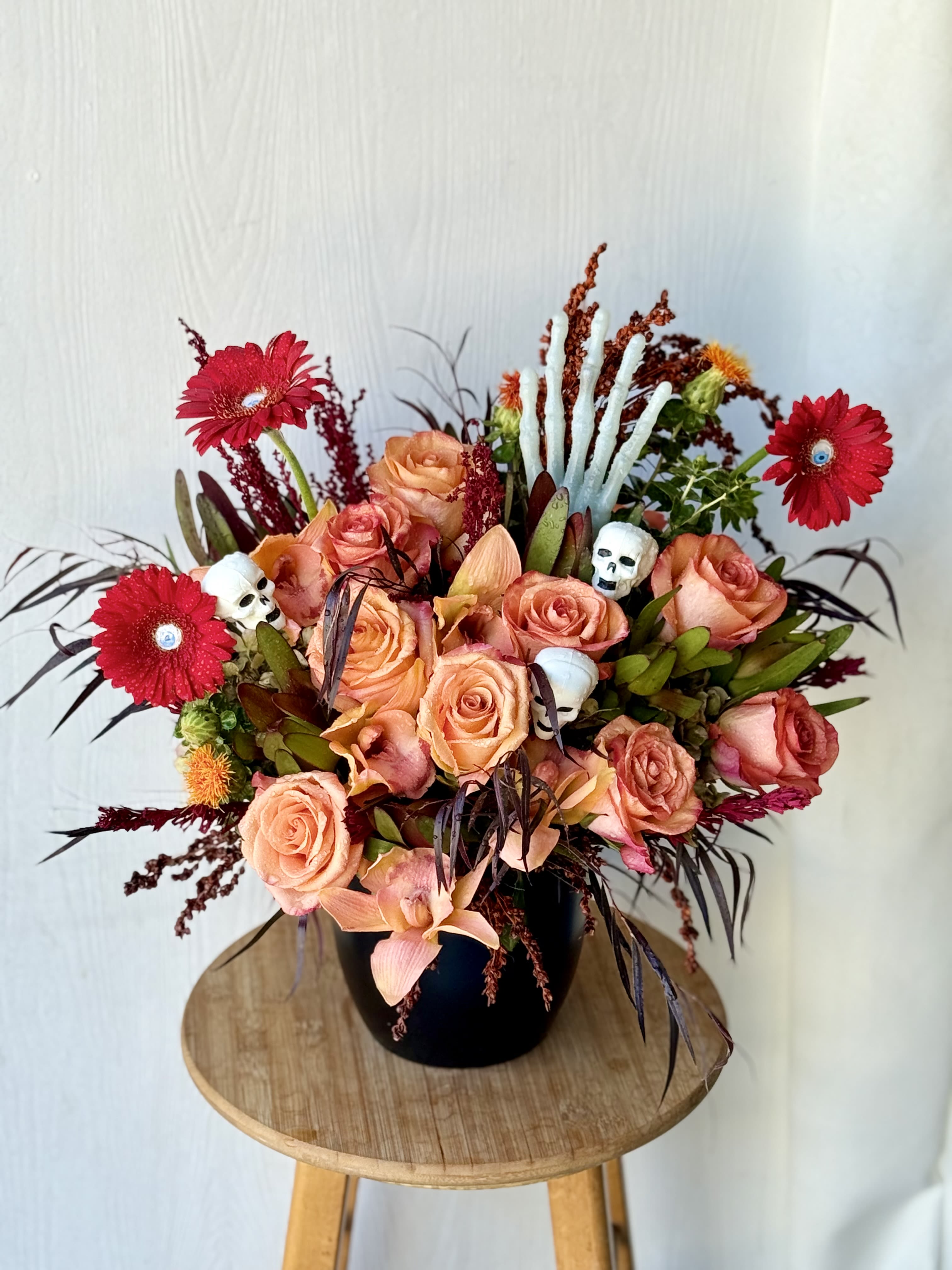 Peach roses and red gerbera daisies in a black vase with skull accents