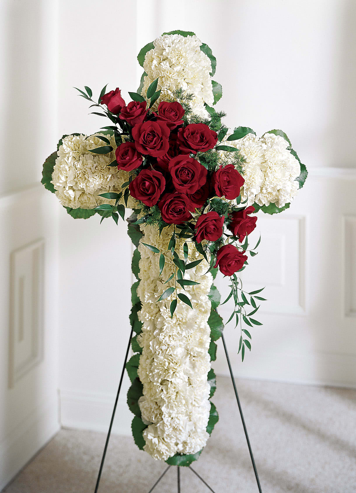 Red roses arranged on a white floral cross with a stand