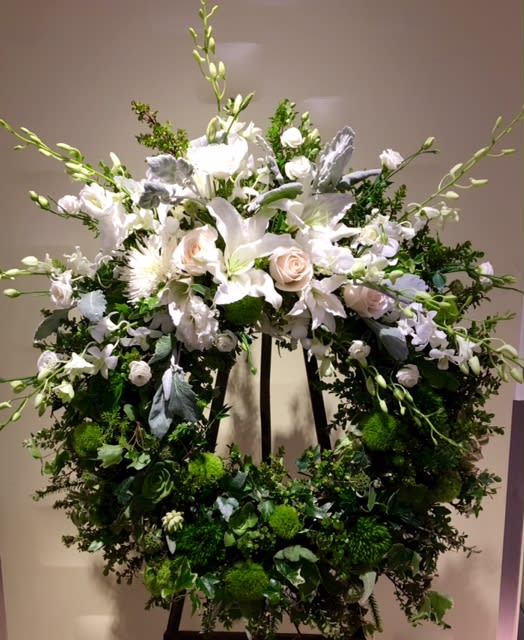 Large white floral wreath on an easel with roses and lilies