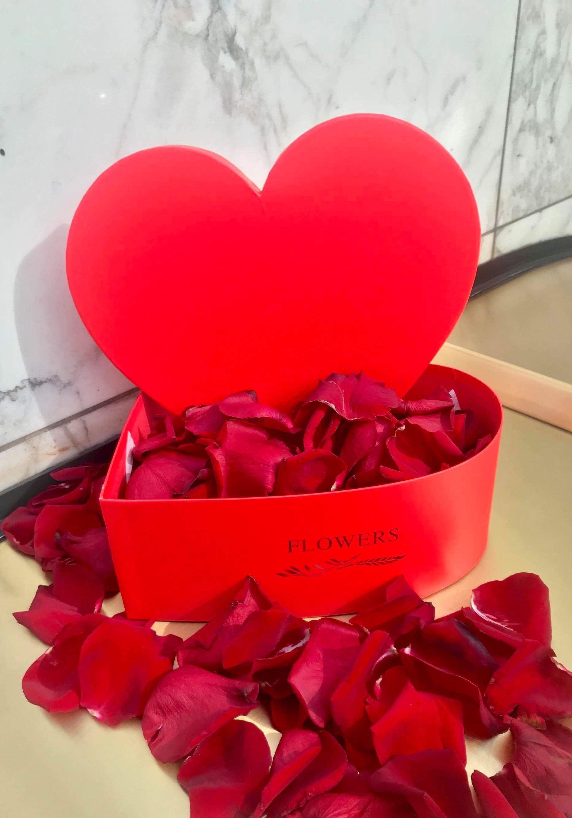 Red heart-shaped gift box filled with rose petals