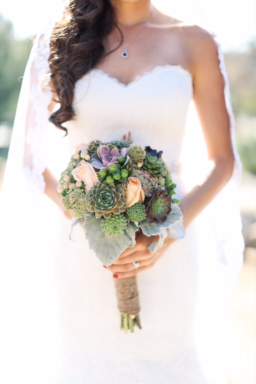 Bride holding a succulent bouquet with pale roses