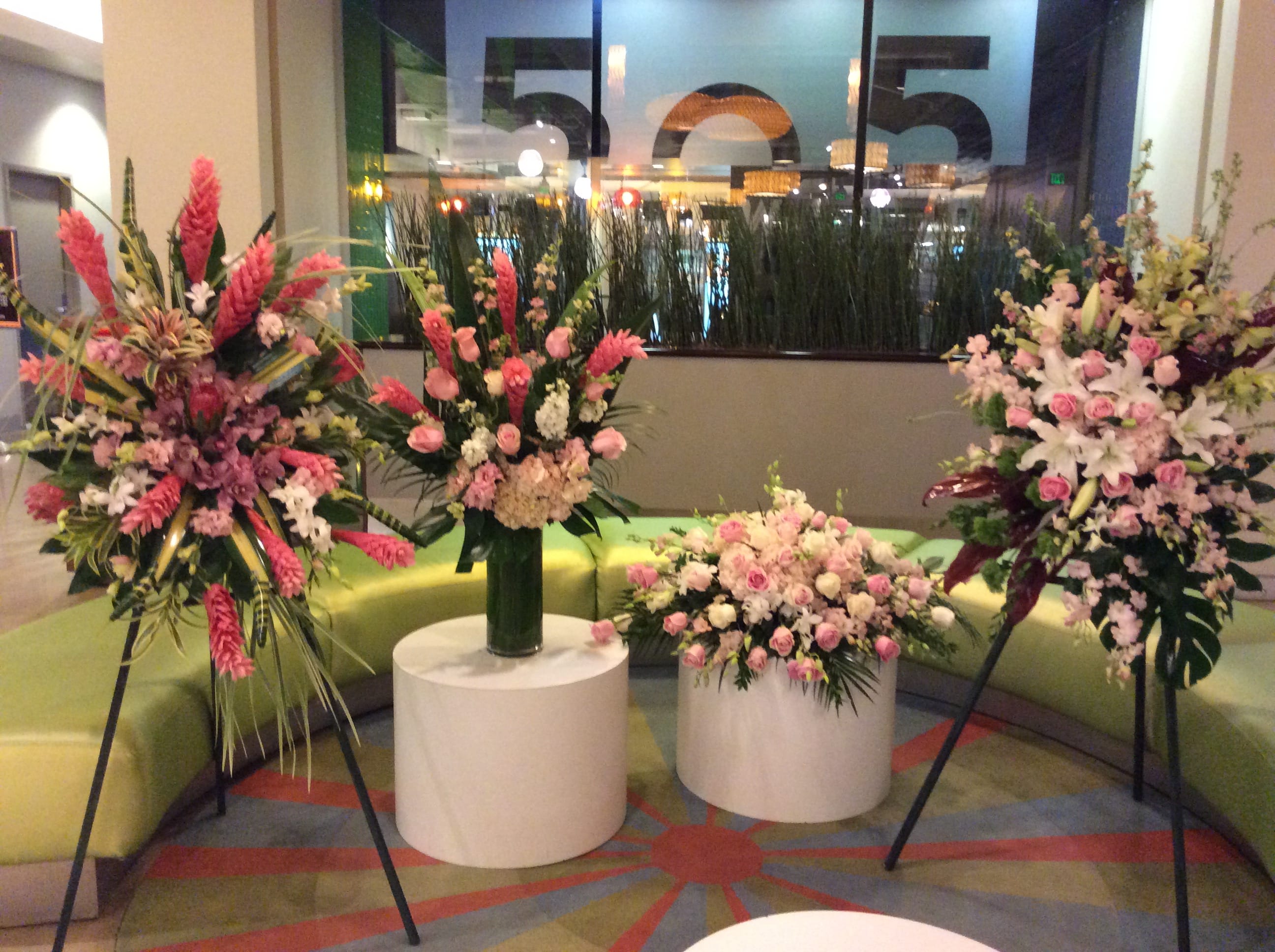 Four pink floral arrangements displayed on stands and pedestals in a lobby