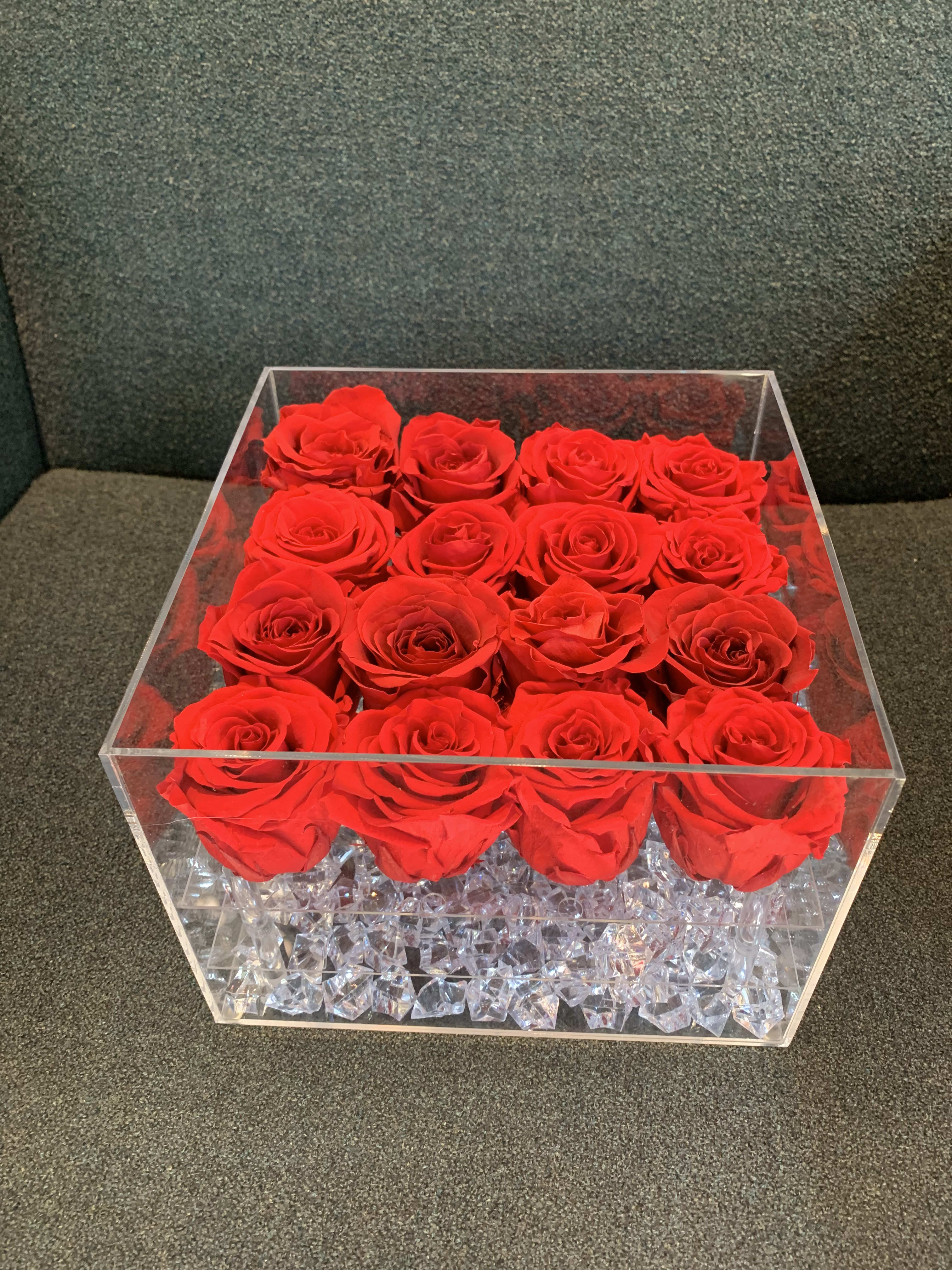 Red roses arranged in a clear square acrylic box with crystal filler