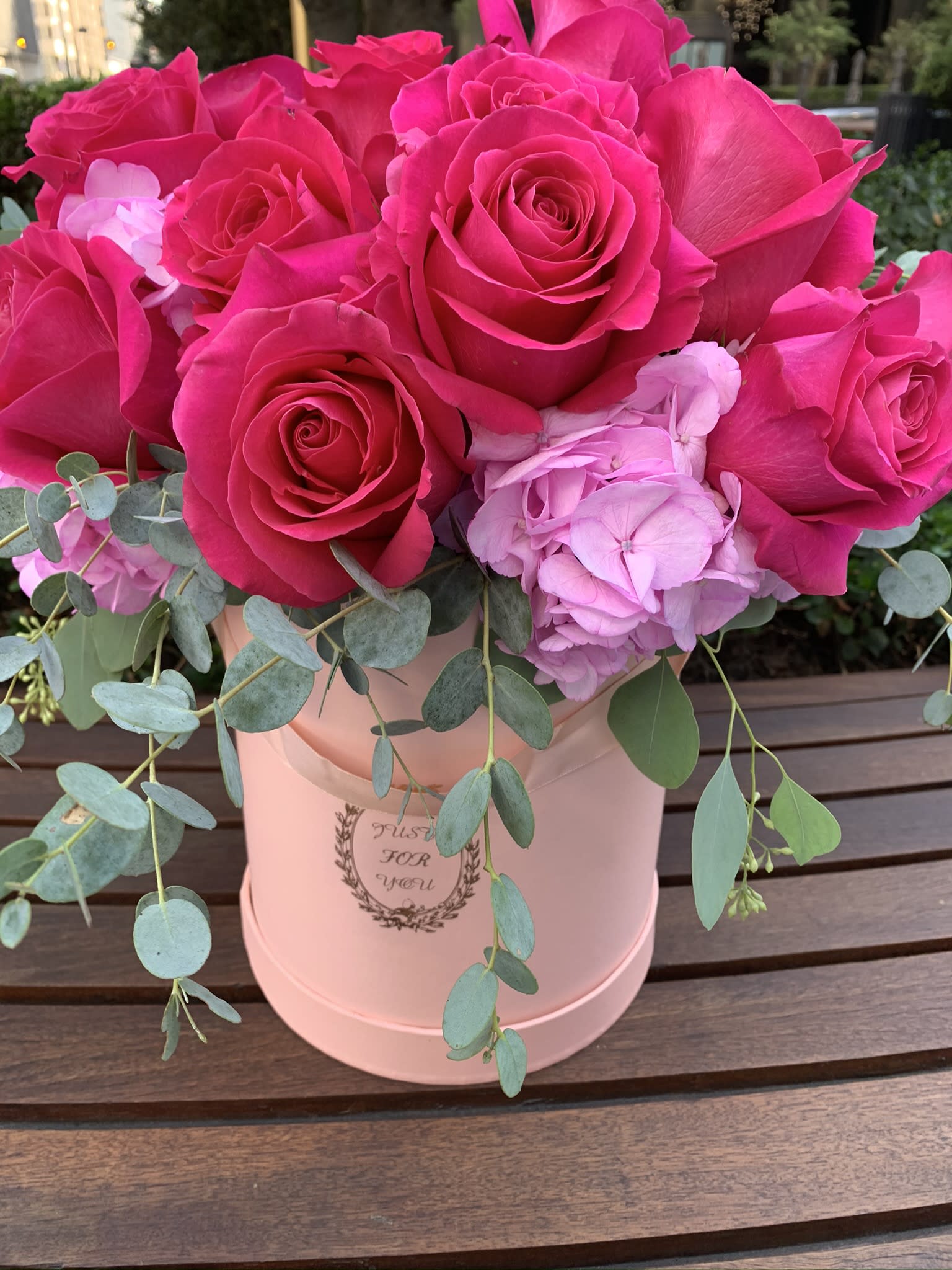 Hot pink roses and pale pink hydrangea in a blush hatbox with trailing eucalyptus.