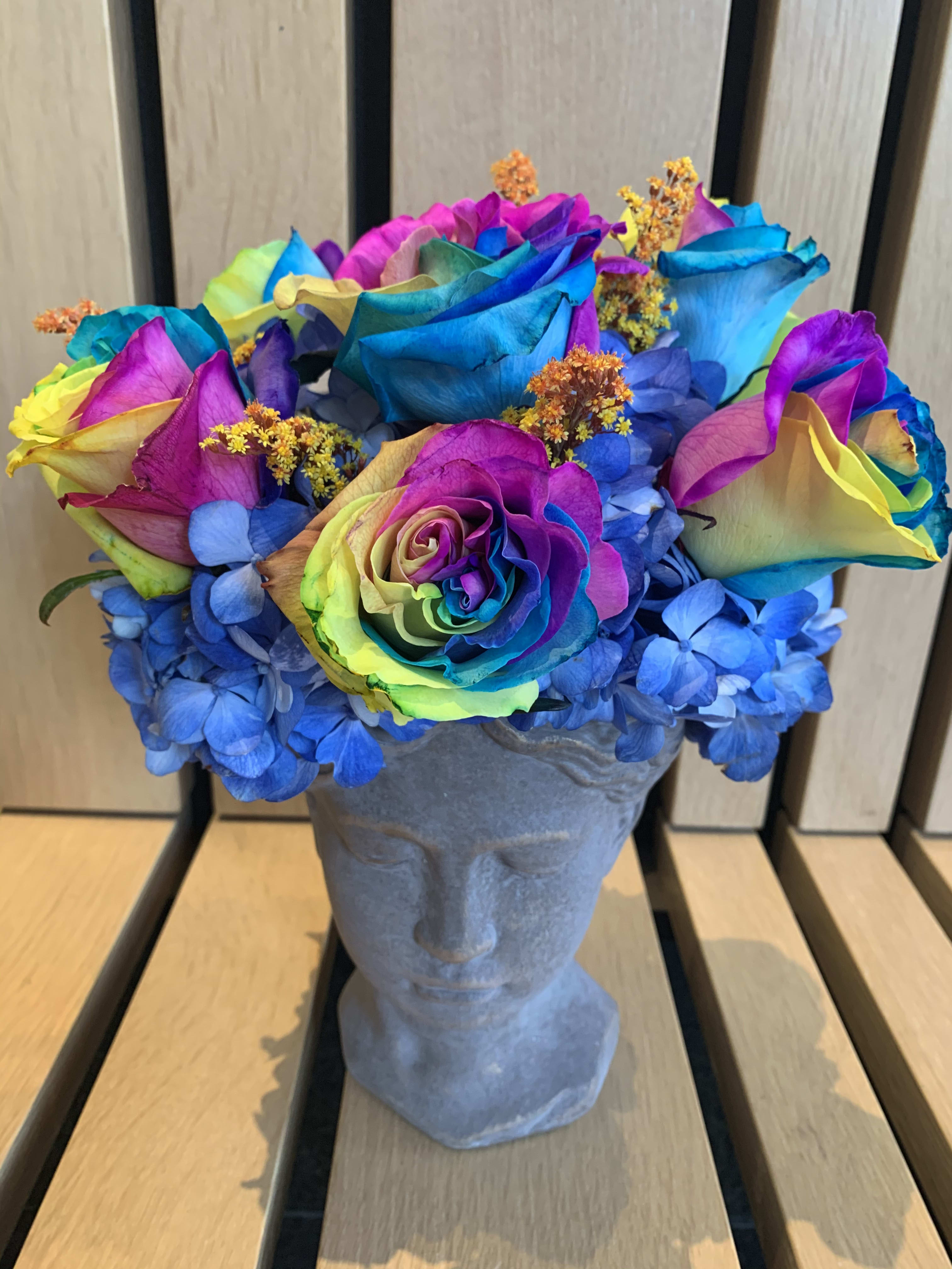 Rainbow-colored roses and blue hydrangeas in a gray bust vase