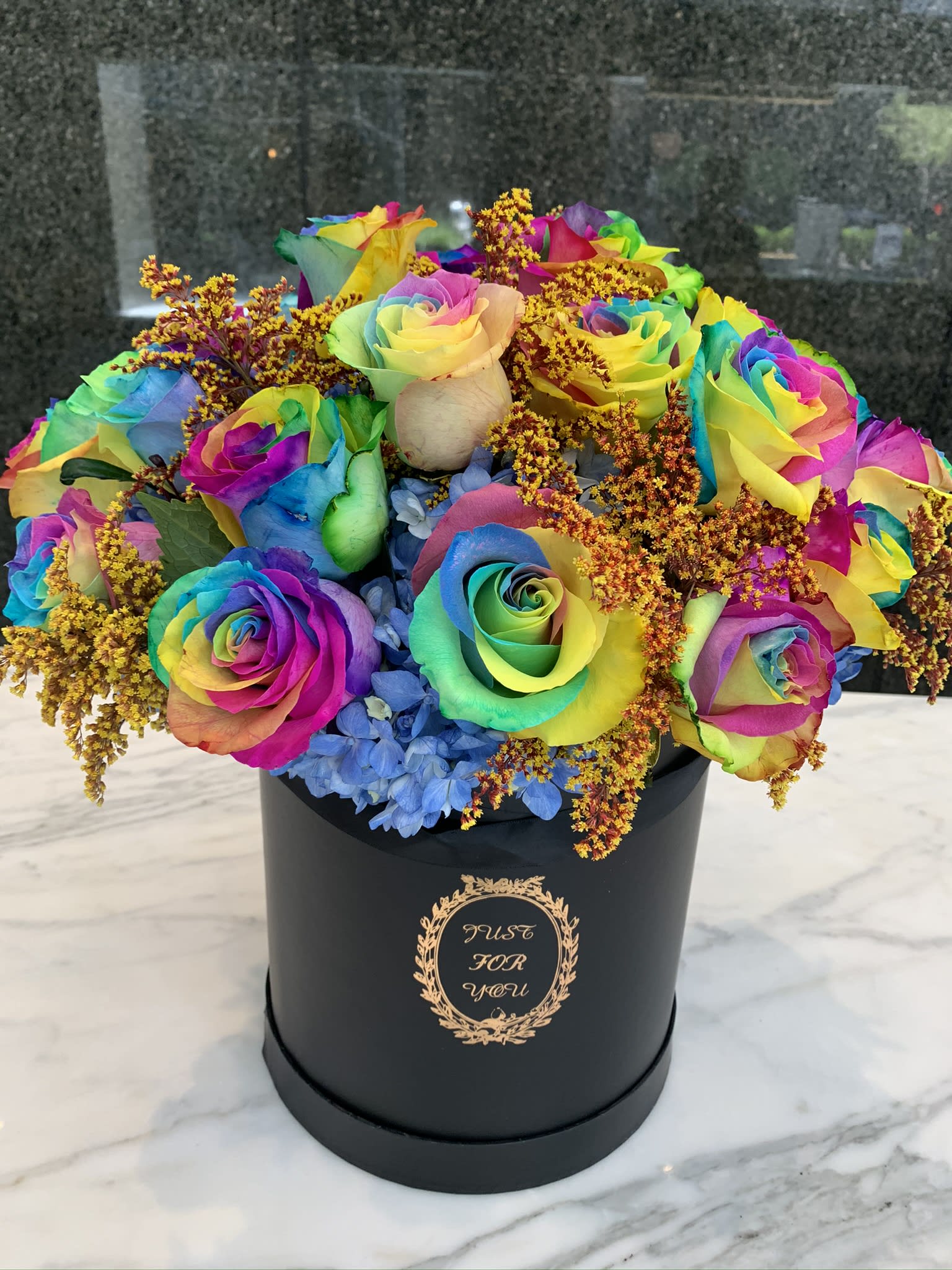 Rainbow roses in a black hatbox with blue hydrangeas