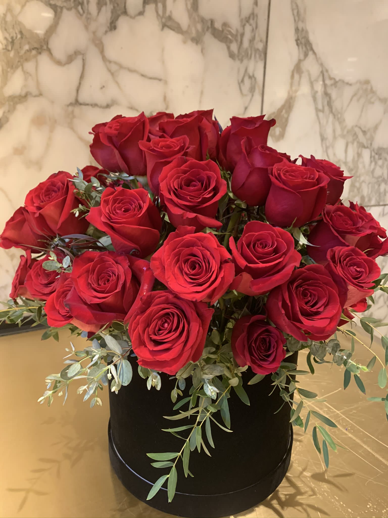 Red roses arranged in a black round box with trailing greenery