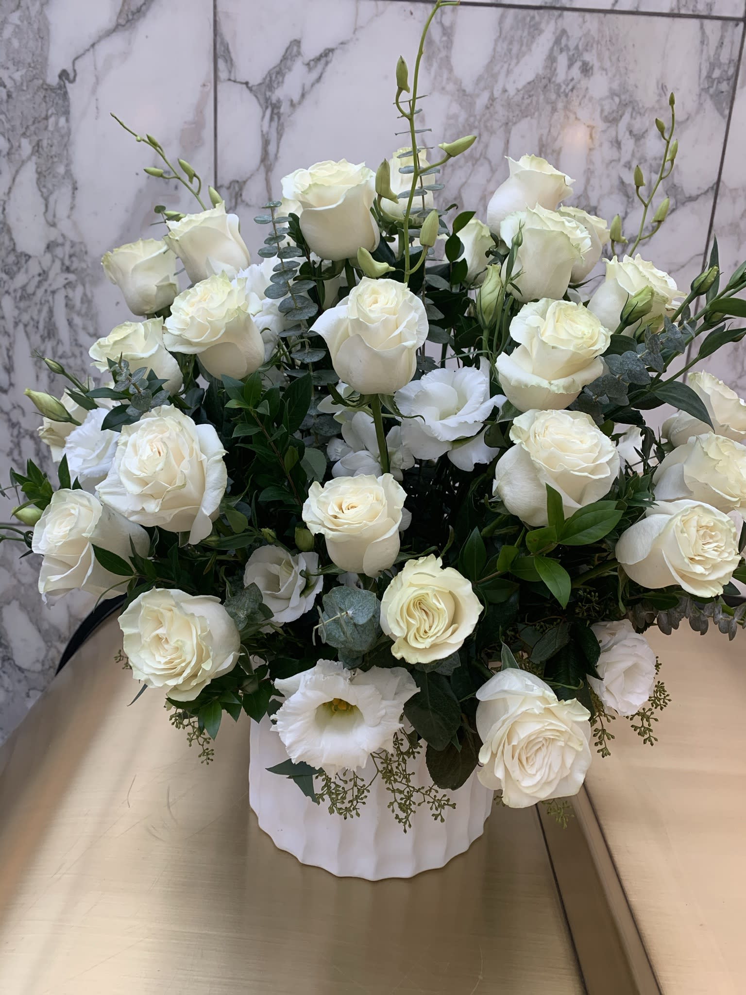 White rose arrangement in a white vase with eucalyptus accents