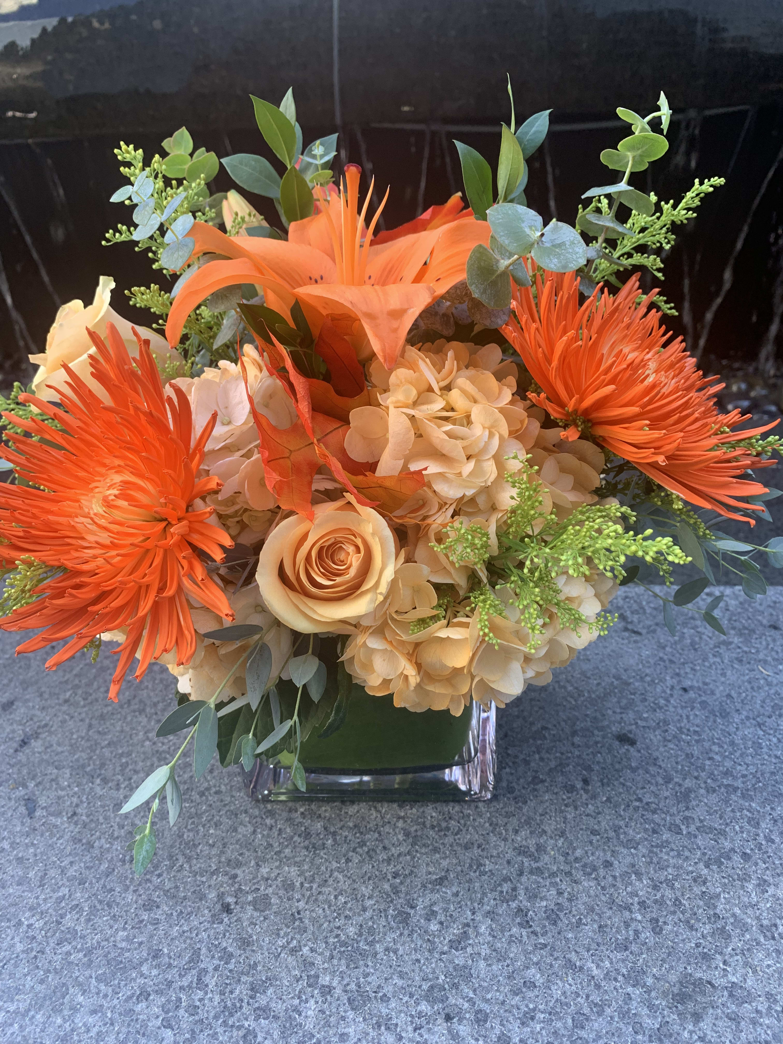 Orange and peach floral arrangement in a clear square vase