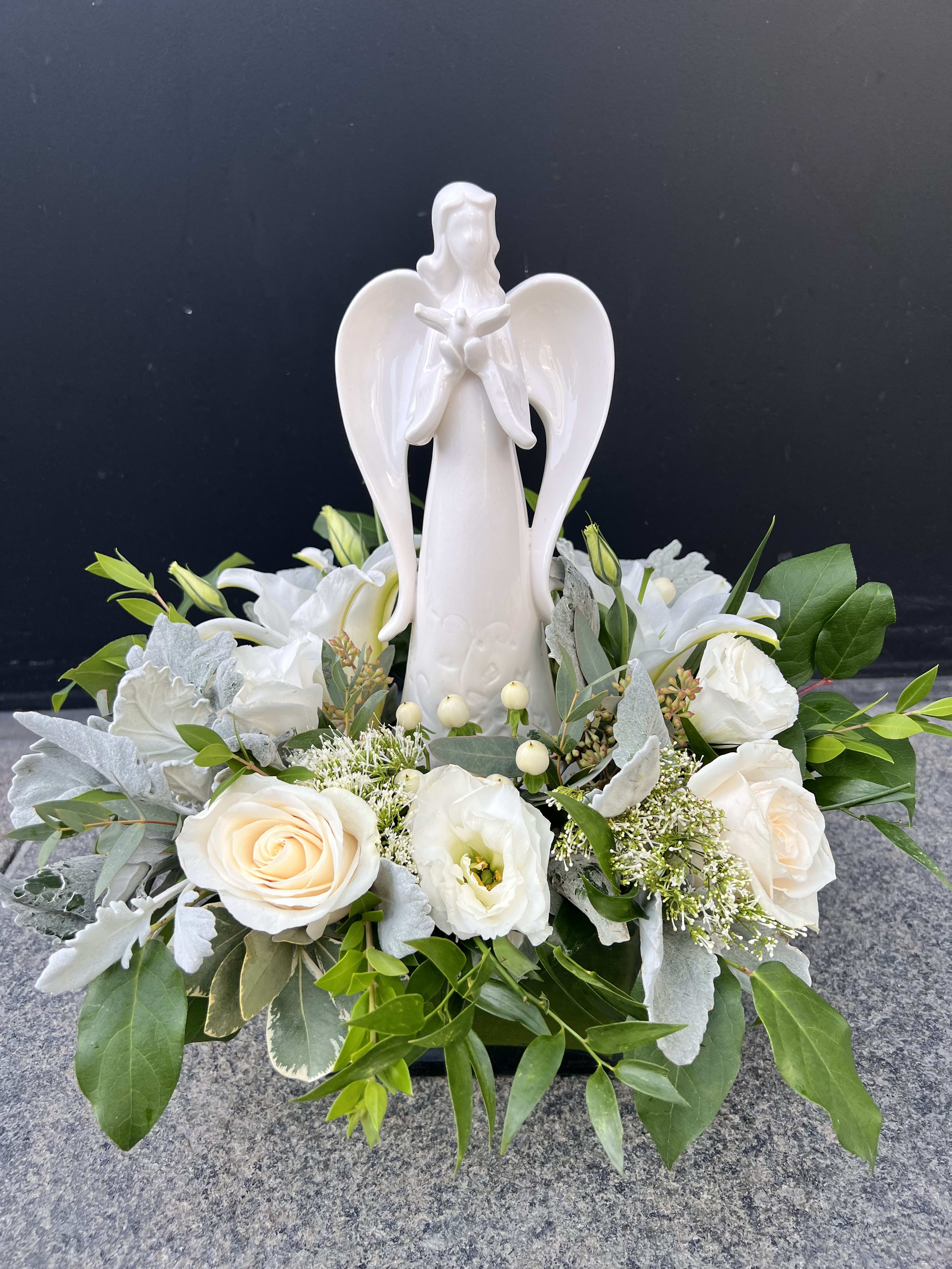 White angel figurine surrounded by white roses and greenery
