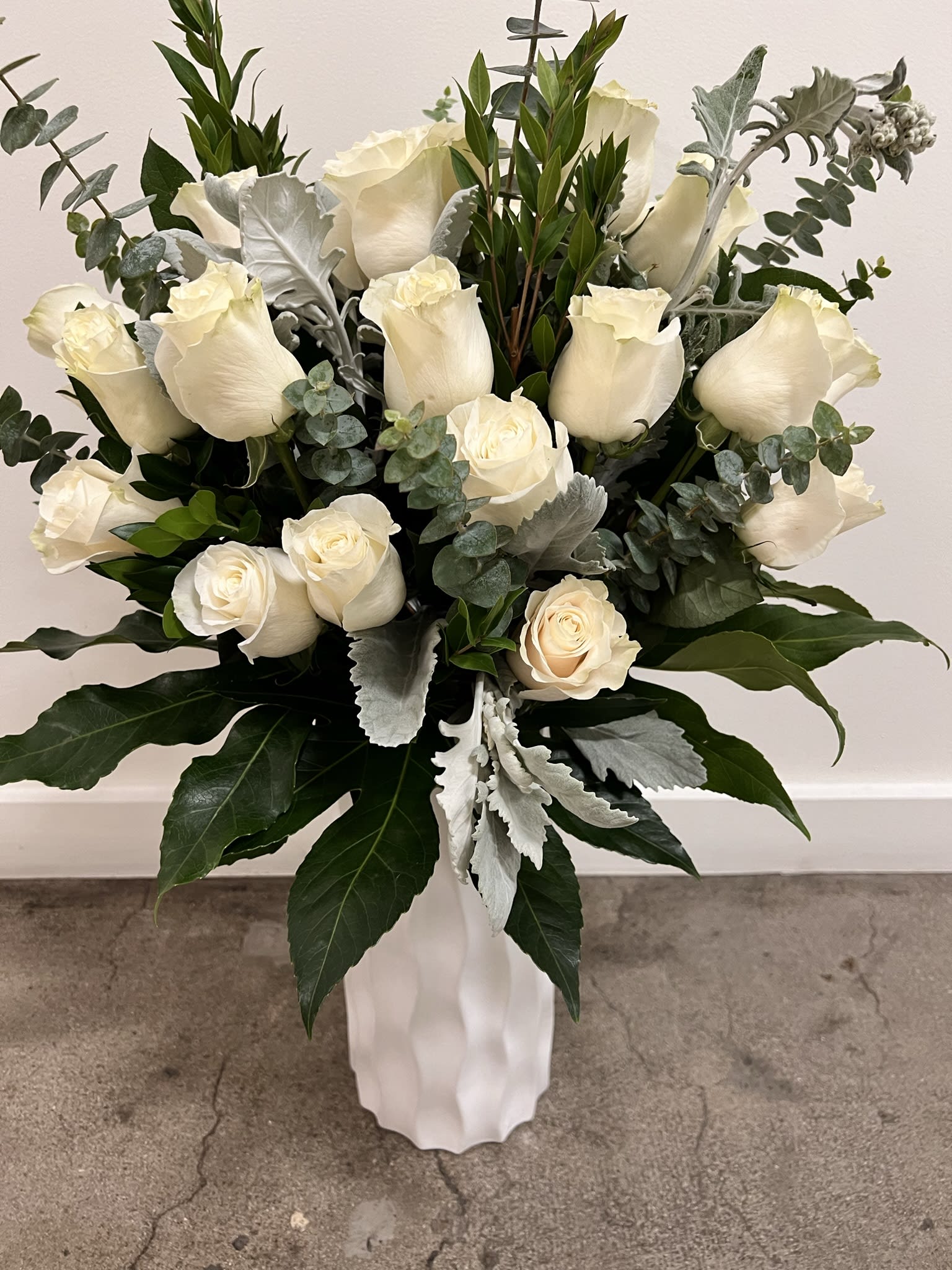 White roses arranged in a tall white vase with silver-green foliage