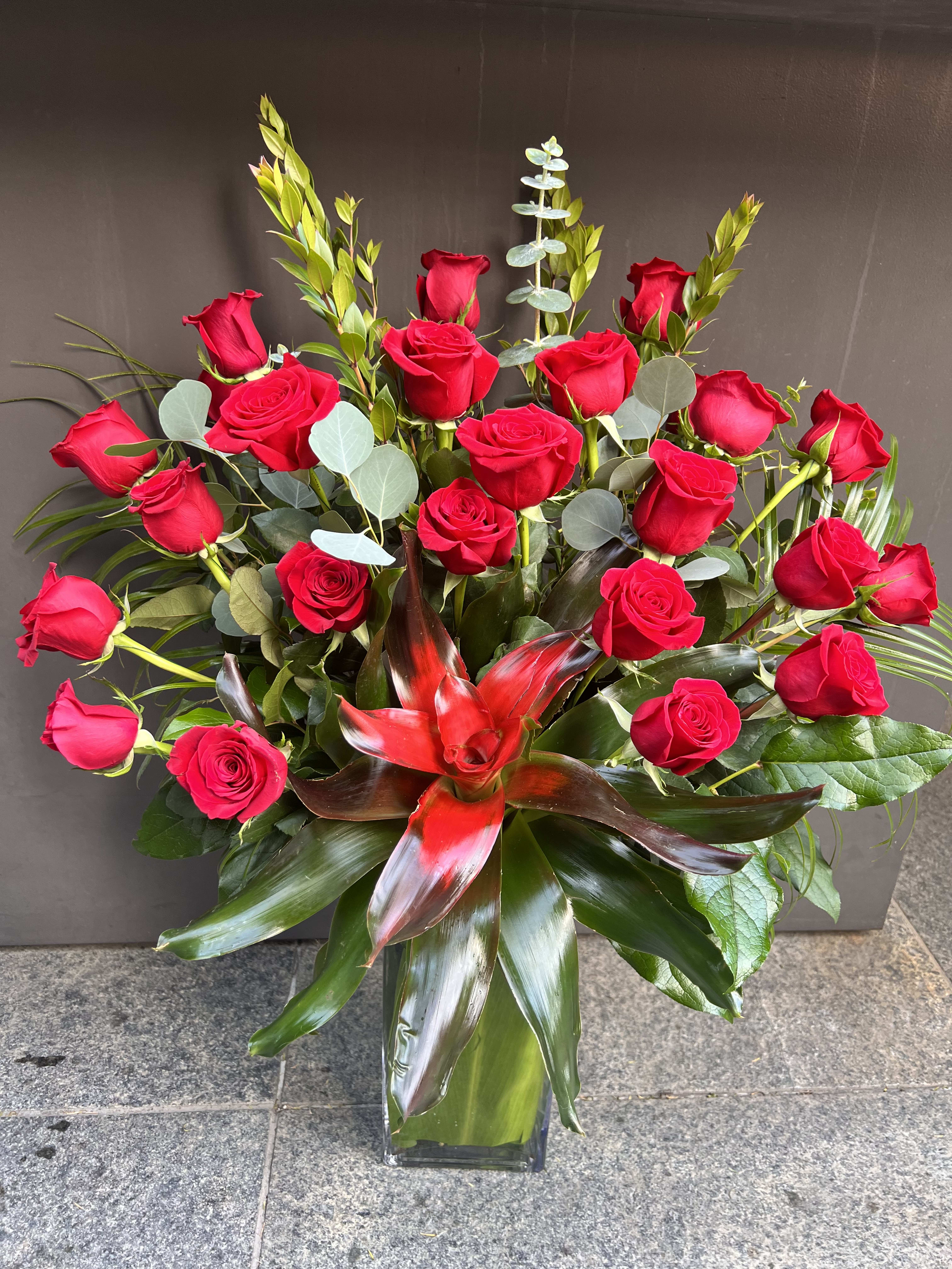 Red roses arranged in a clear glass vase with tropical foliage