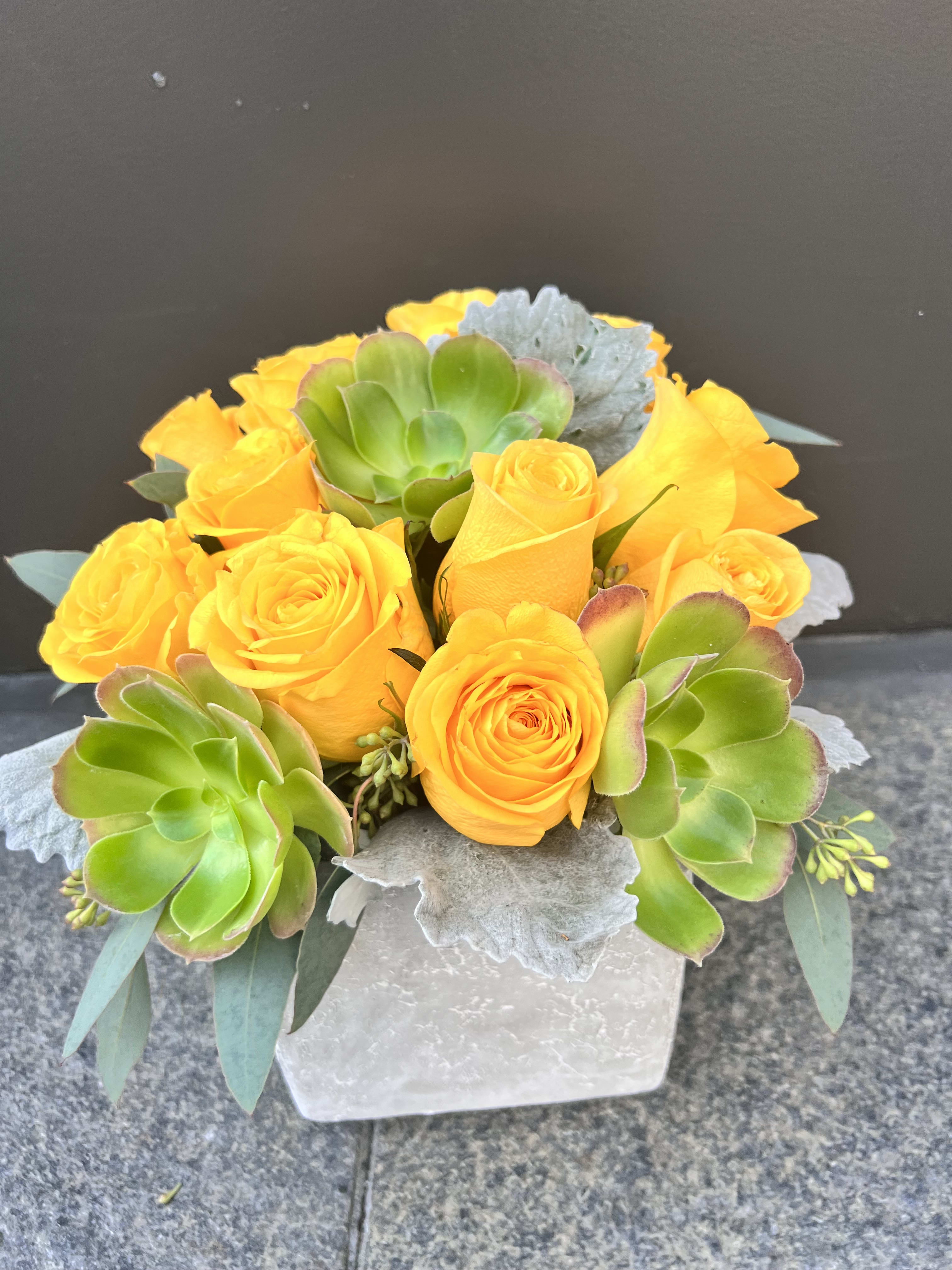 Yellow roses and green succulents in a white square vase