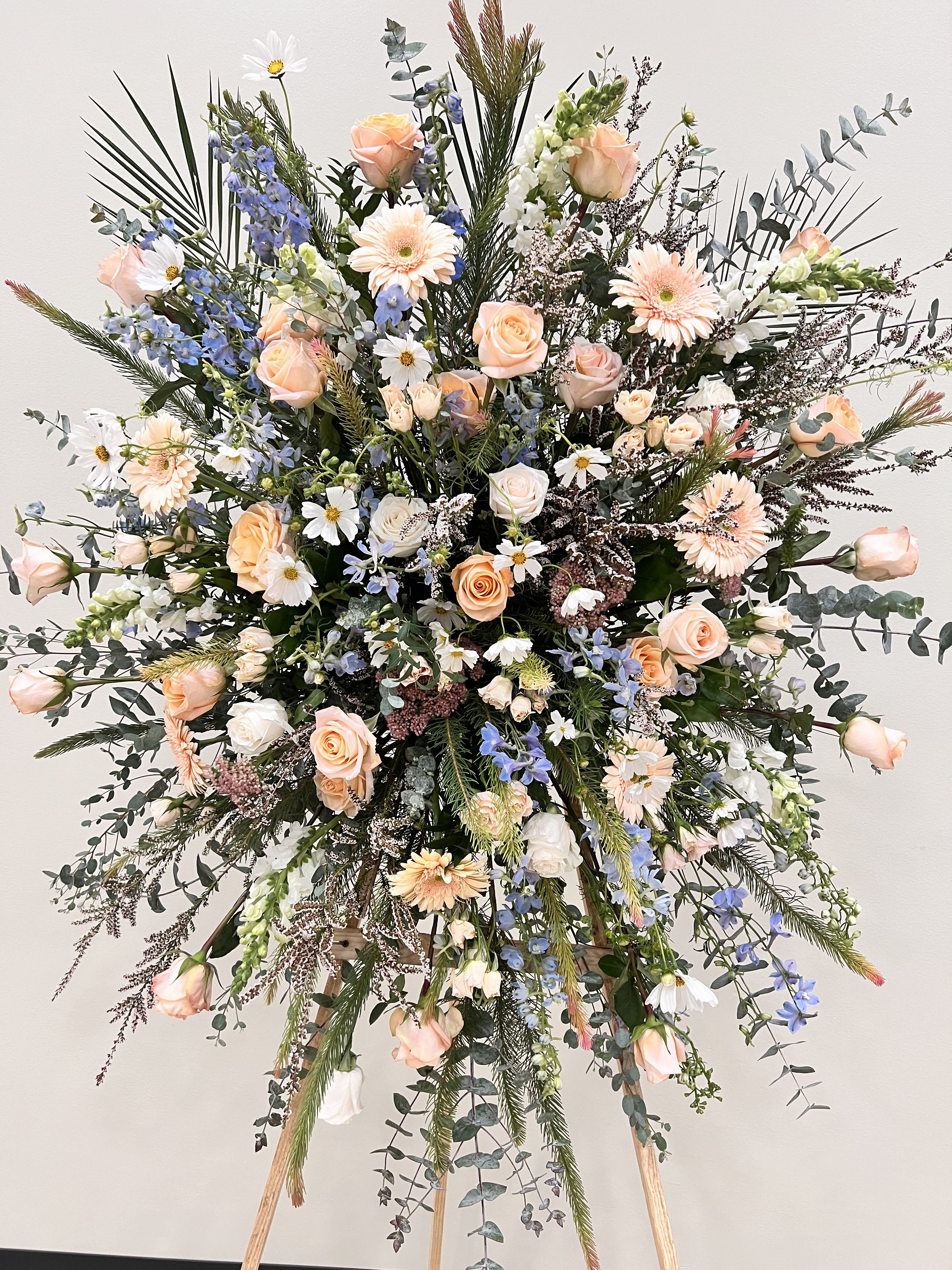 Large standing floral spray with peach roses and blue delphinium
