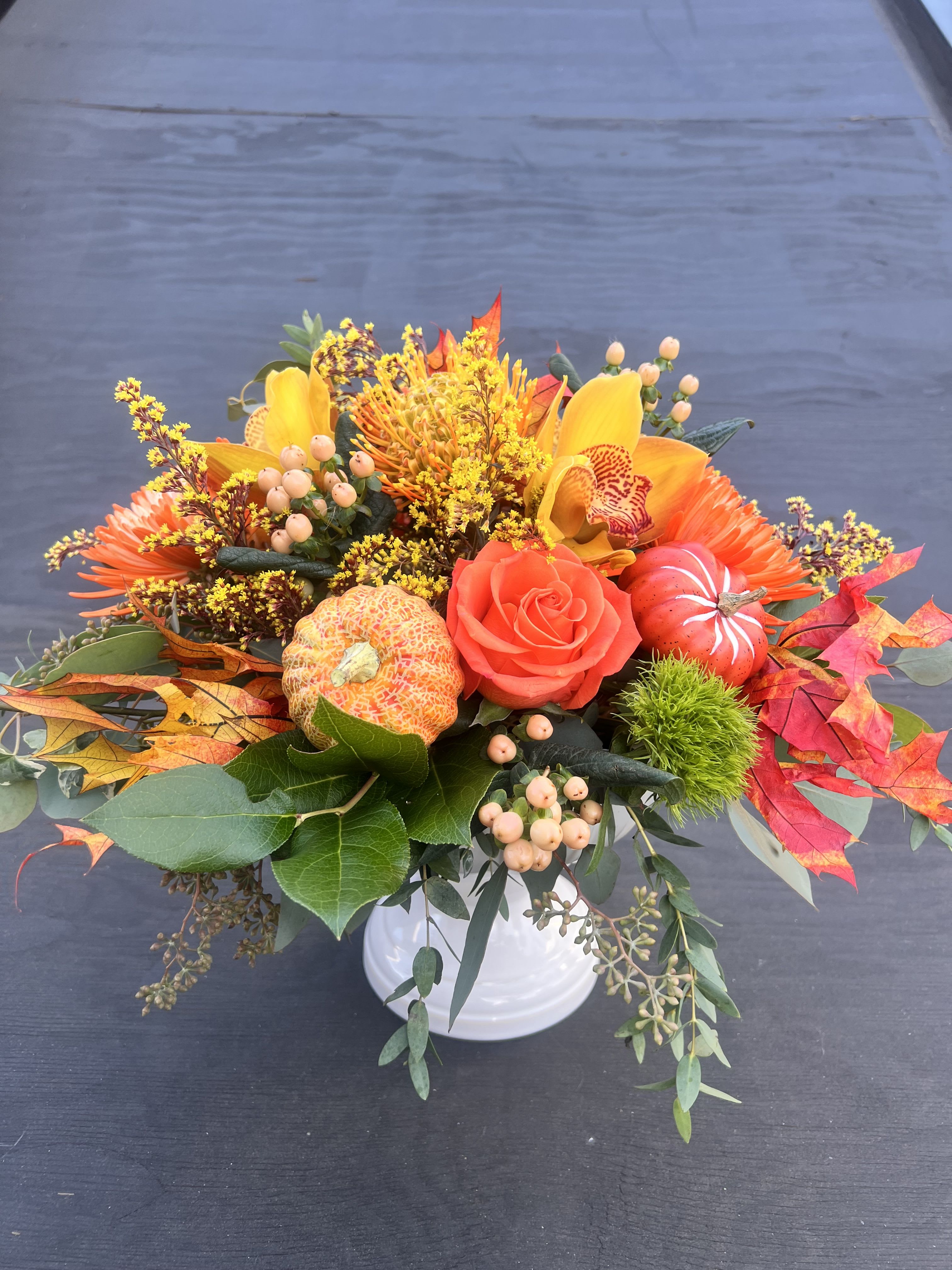 Autumn floral arrangement in a white vase with orange and yellow blooms