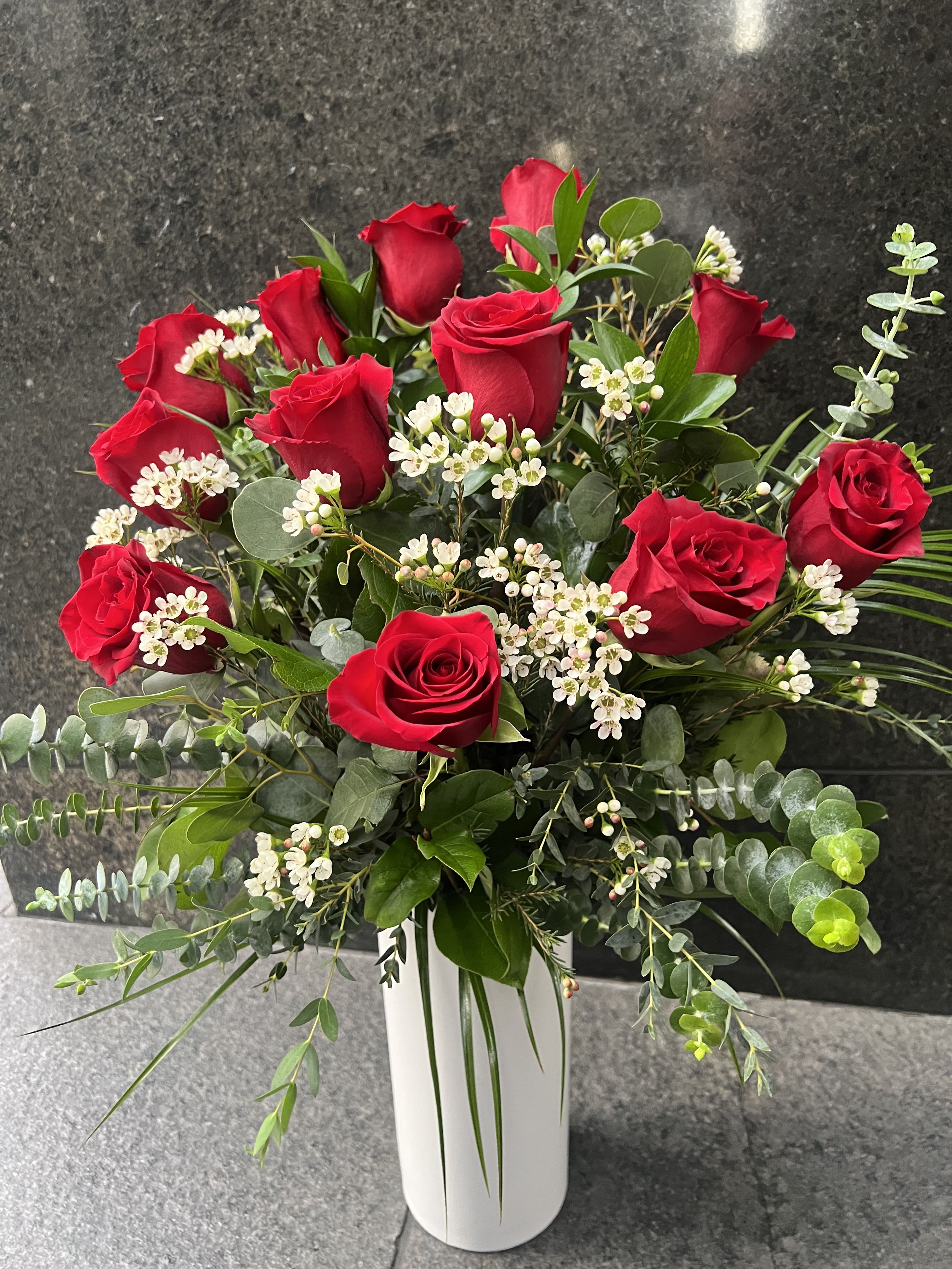 Red roses arranged in a white vase with white filler flowers and greenery