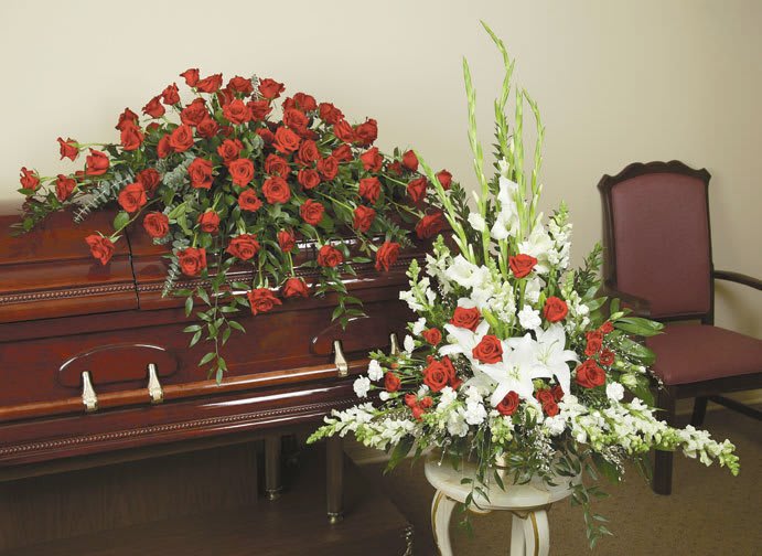Casket spray of red roses and white lilies beside a matching standing arrangement