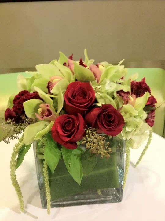 Red roses and pale green orchids in a square glass vase