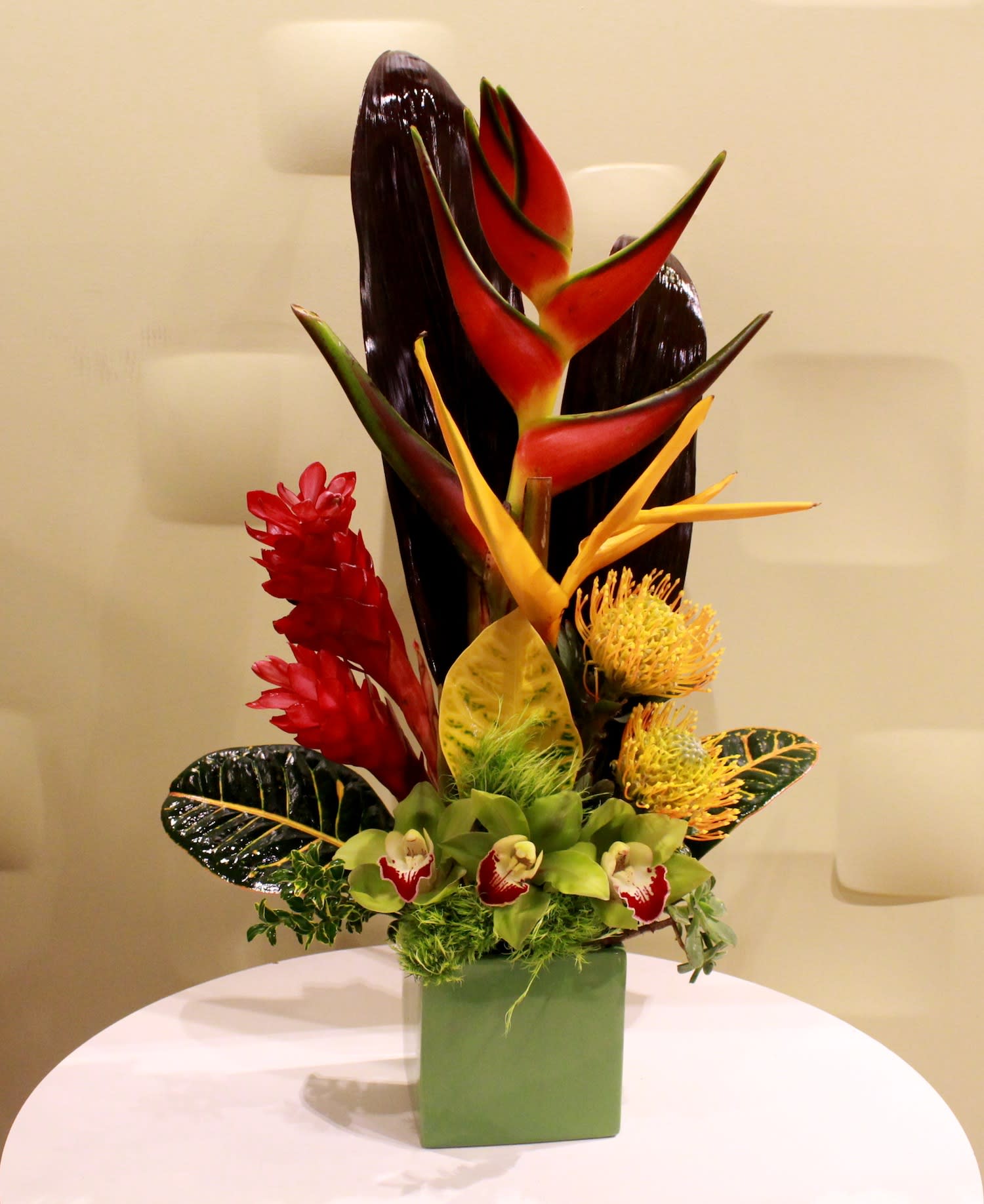 Tropical flower arrangement in a green square vase with red and yellow blooms