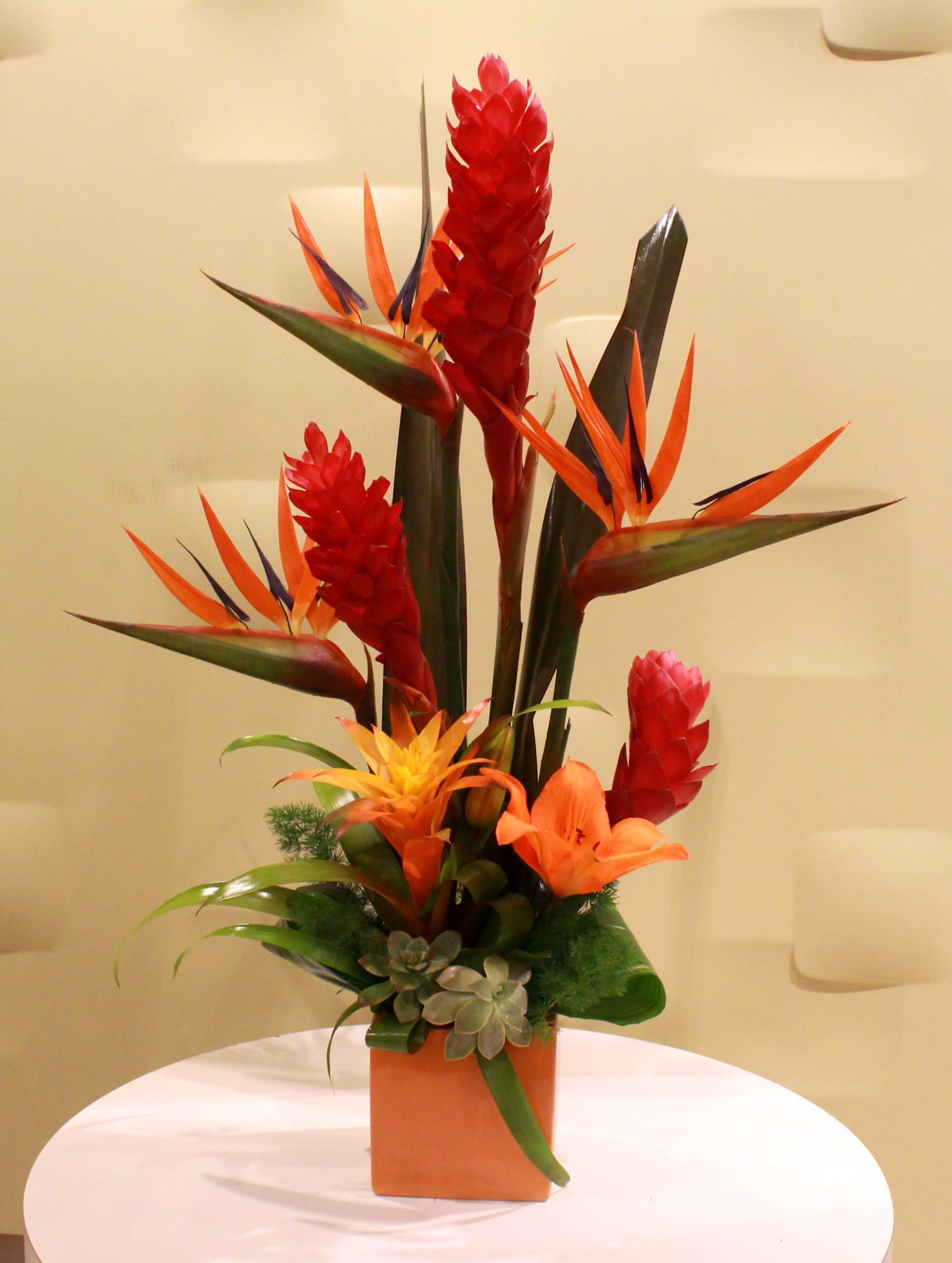 Tropical flower arrangement with red ginger and orange bird of paradise in a square vase