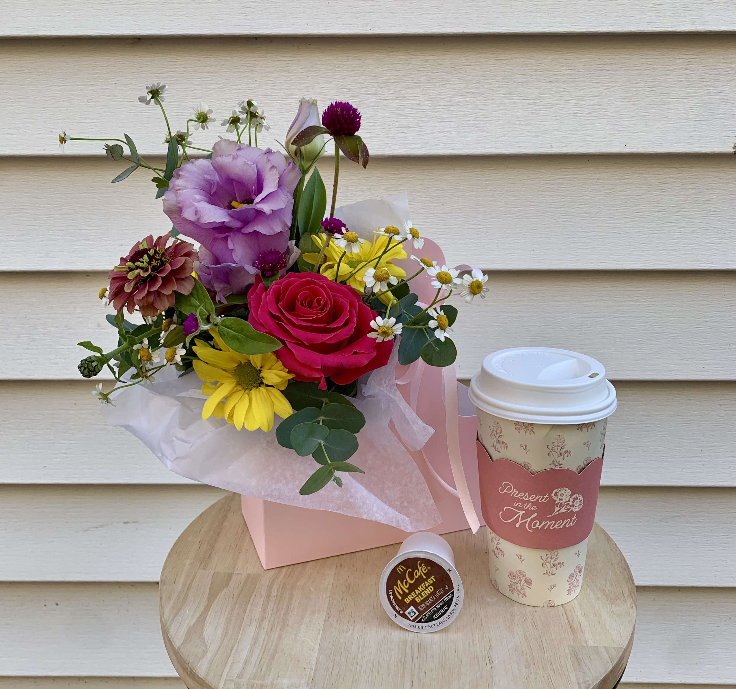 Mixed bouquet in a pink box with a coffee cup and coffee pod beside it