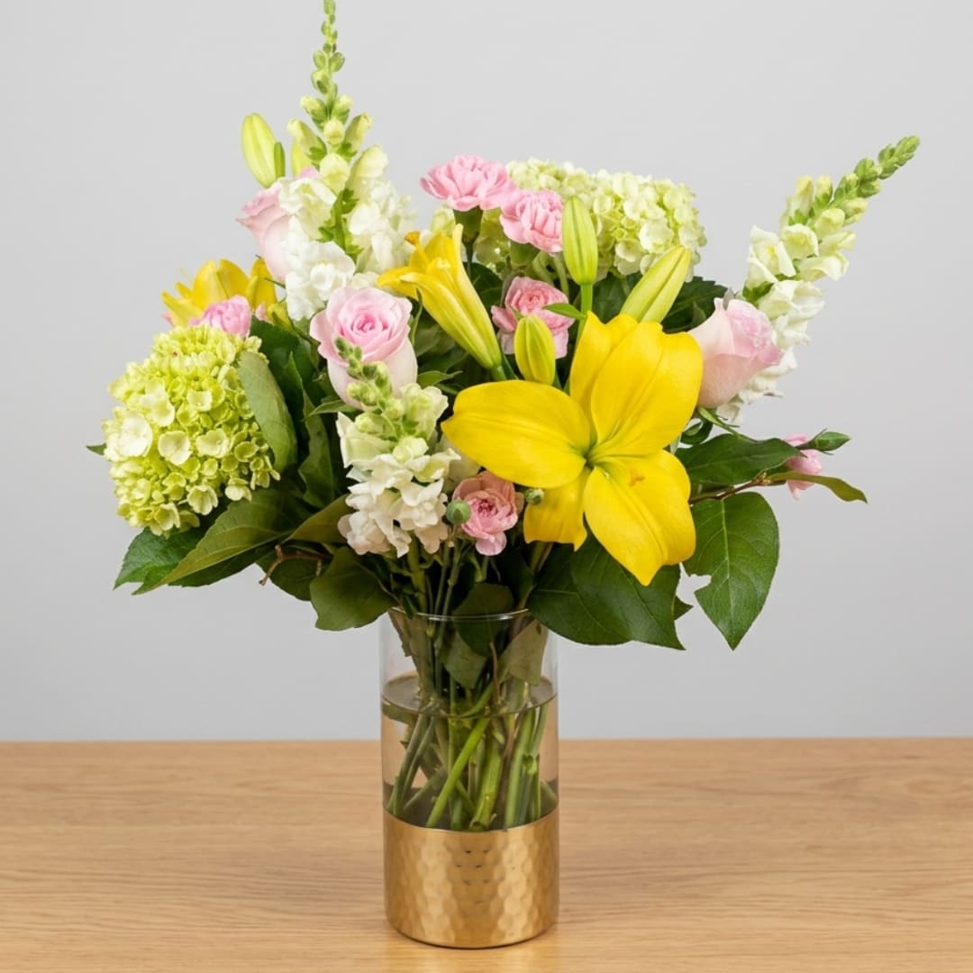 Bouquet of yellow lilies, pink roses, and white blooms in a glass vase