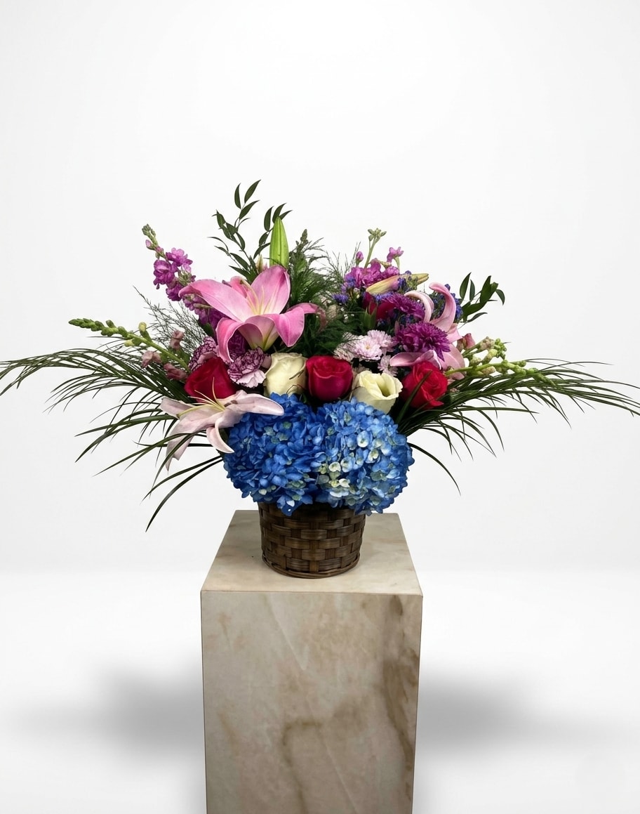 Mixed bouquet with pink lilies, roses, and blue hydrangea in a woven basket