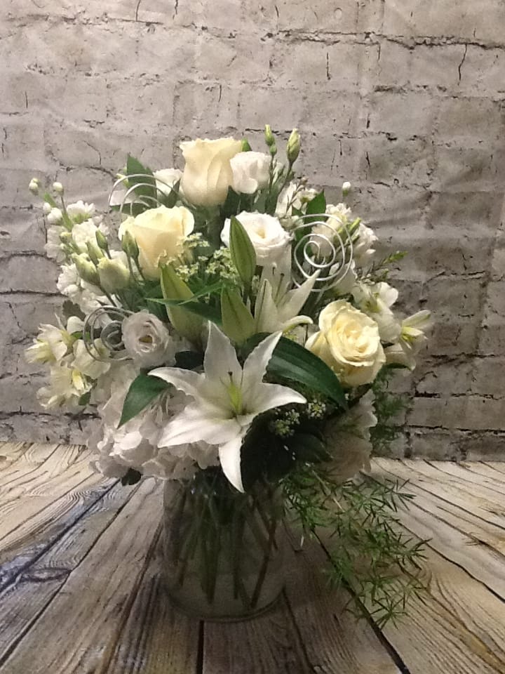 White and cream floral arrangement with lilies and roses in a glass vase
