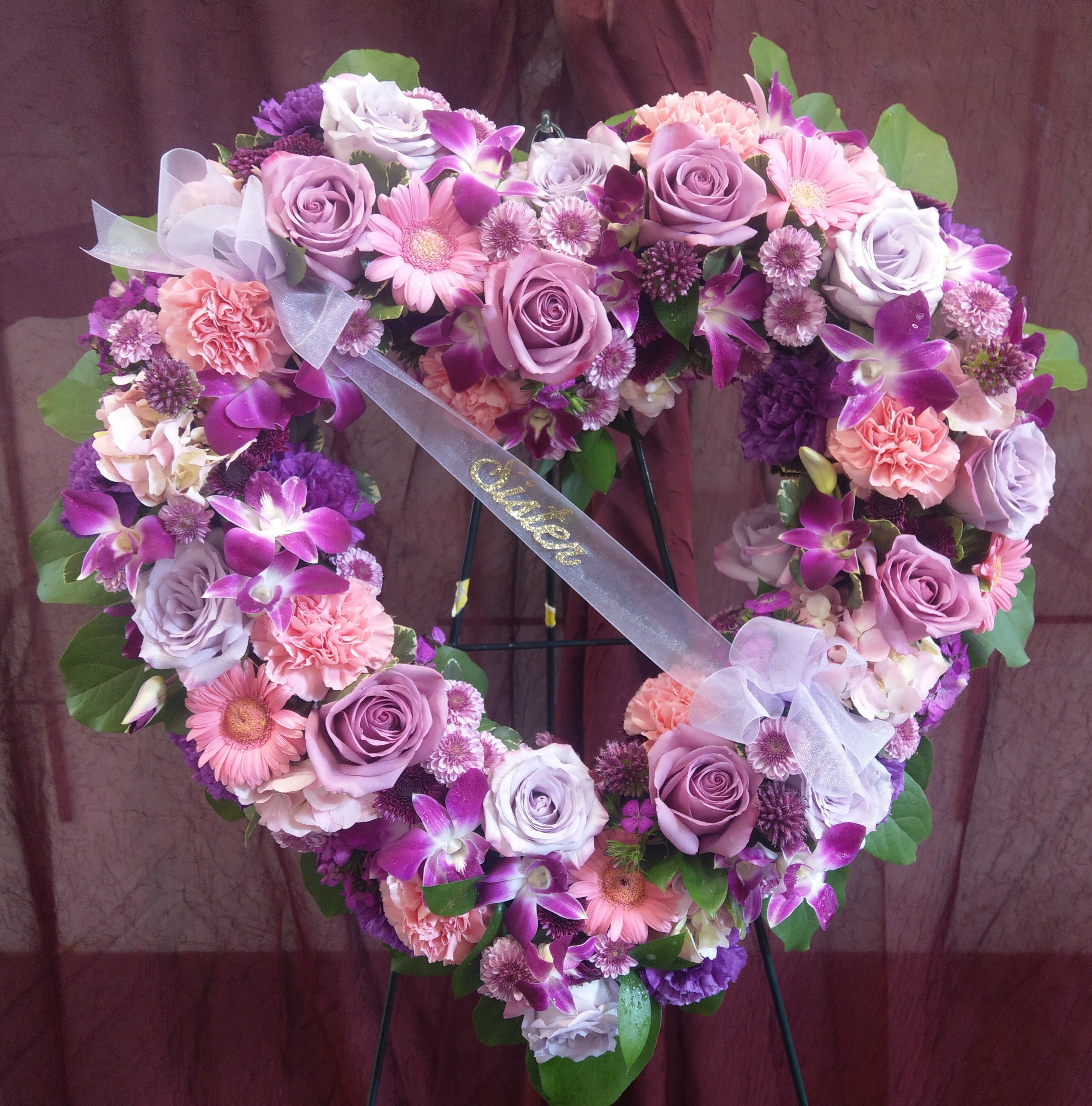 Heart-shaped floral wreath with pink and purple roses, orchids, and daisies