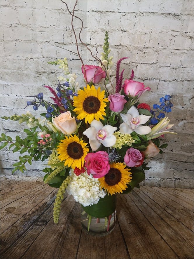 Mixed bouquet with sunflowers, pink roses, and white orchids in a glass vase