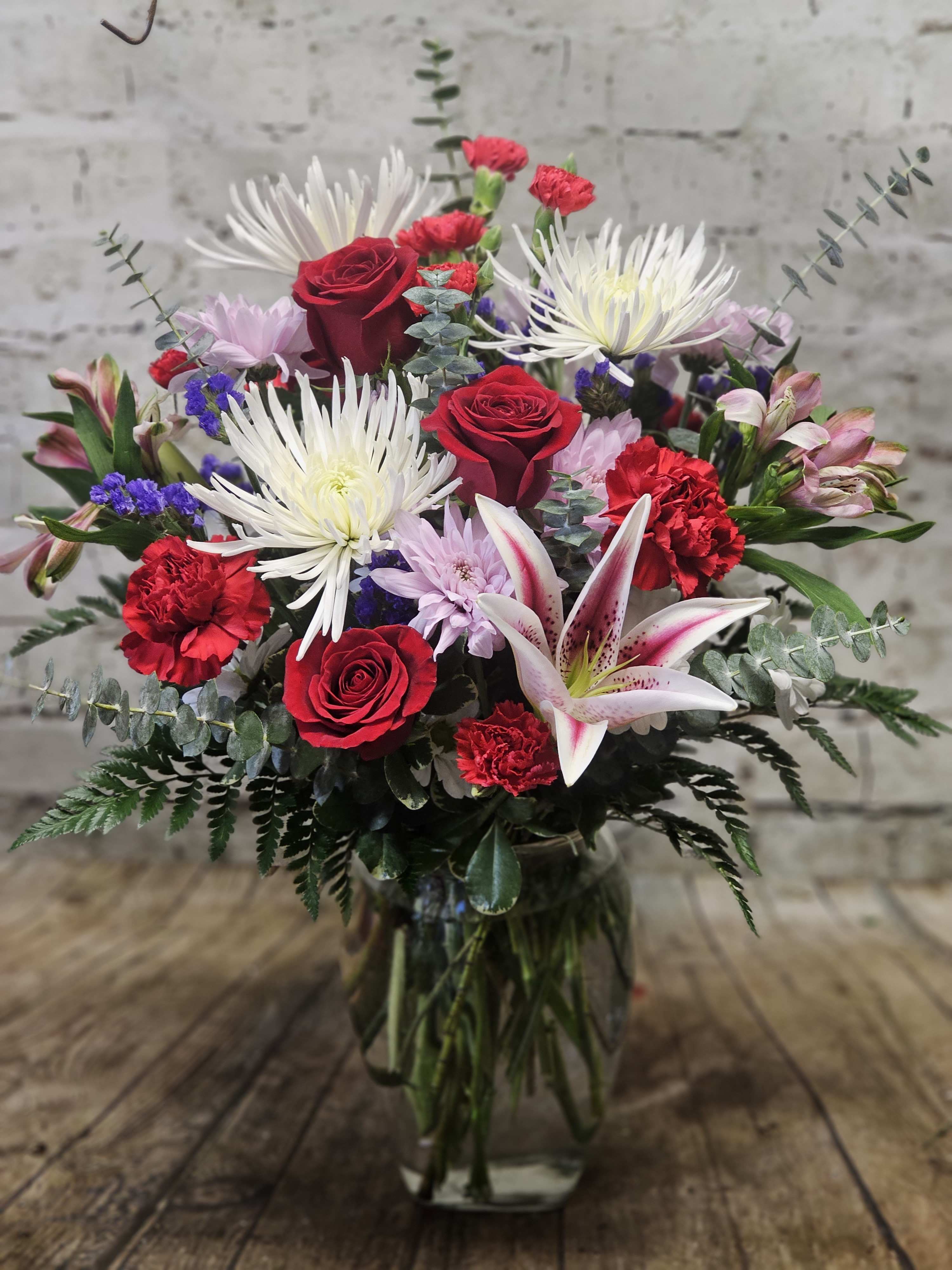 Mixed bouquet with red roses, white lilies, and pink flowers in a glass vase