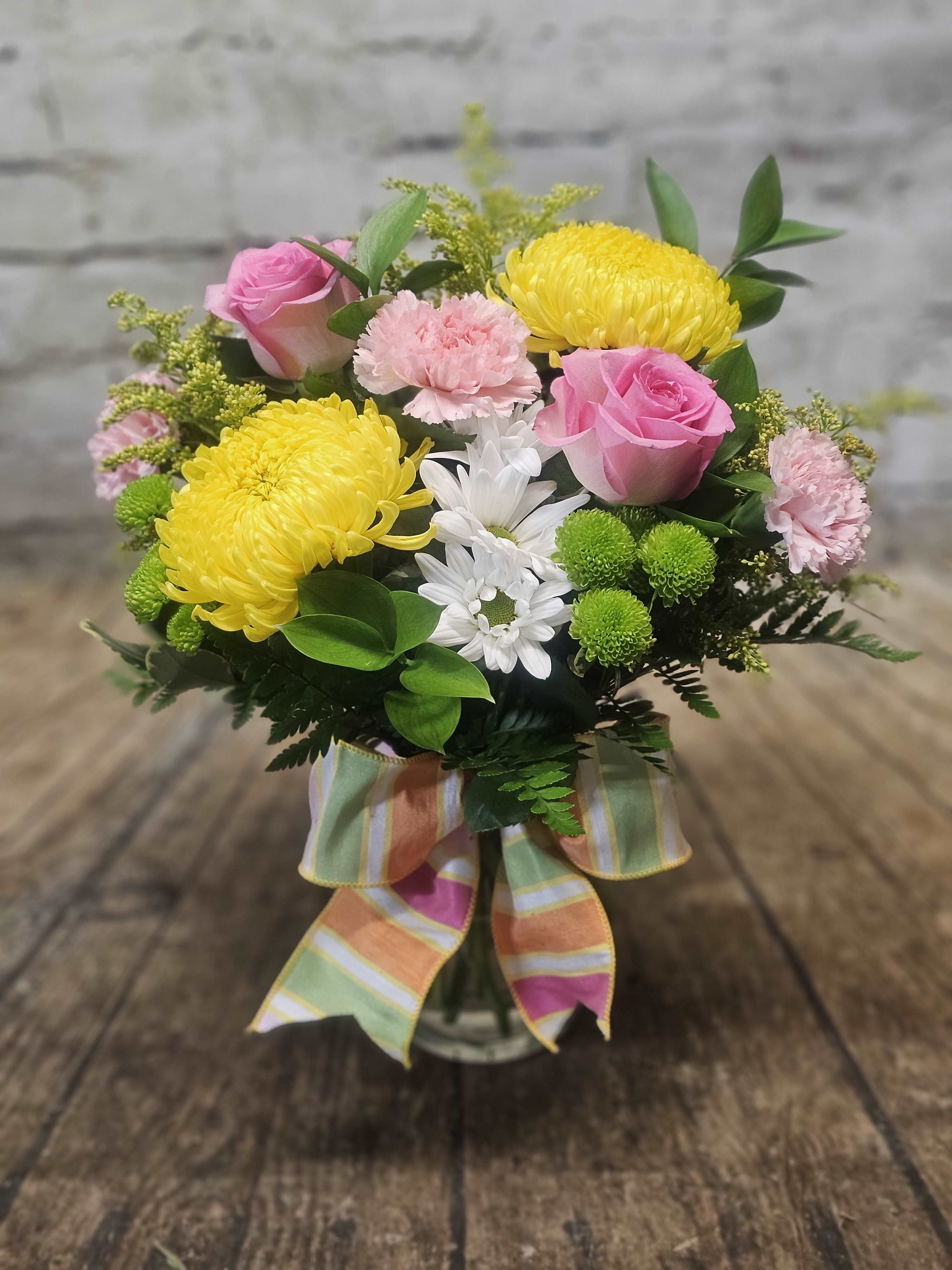 Pink roses and yellow chrysanthemums in a glass vase with a striped ribbon