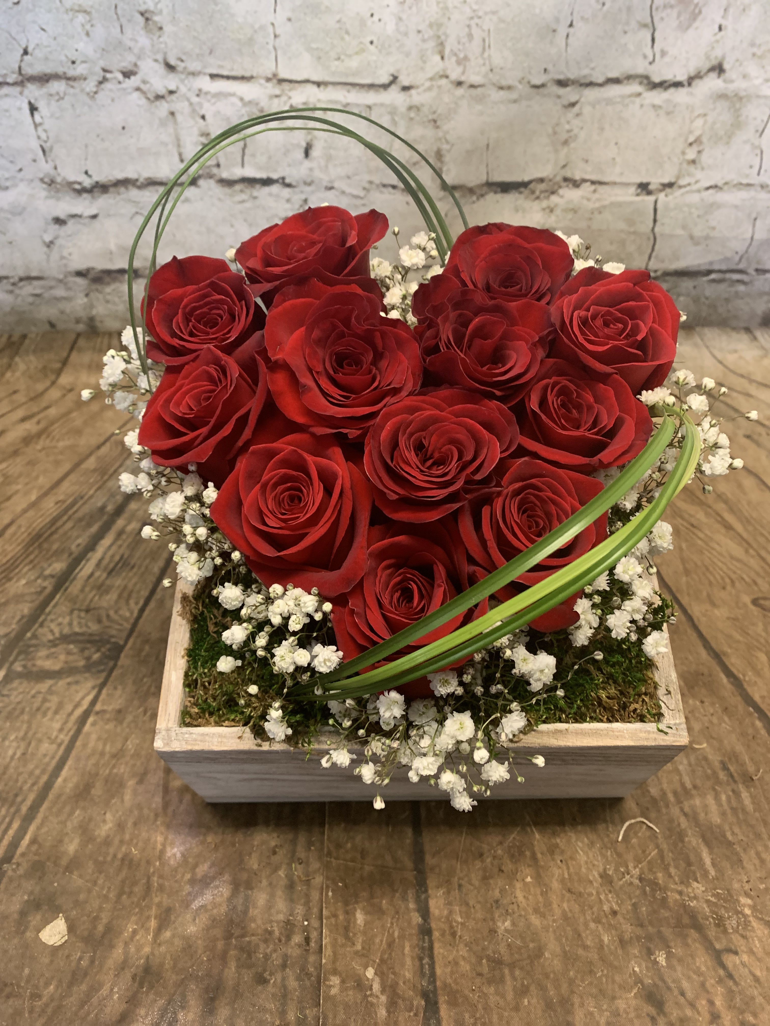 Red roses arranged in a square wooden box with white baby's breath