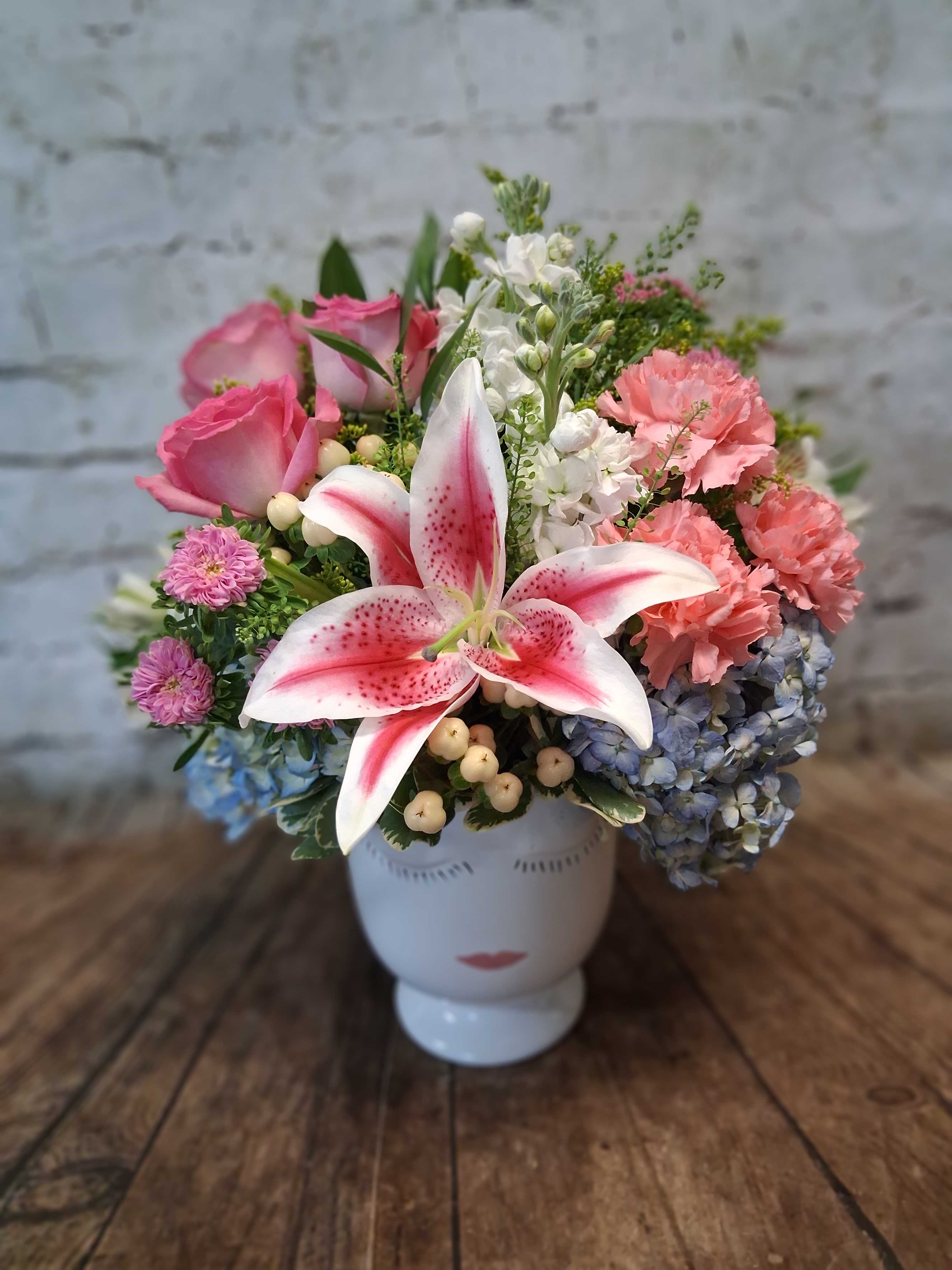 Mixed bouquet with pink roses, lilies, hydrangeas, and carnations in a white vase