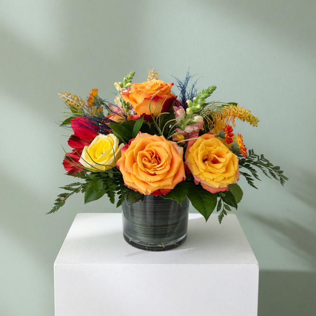 Colorful rose arrangement in a glass vase on a white pedestal