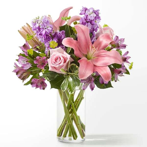 Pink lilies and purple flowers in a clear glass vase