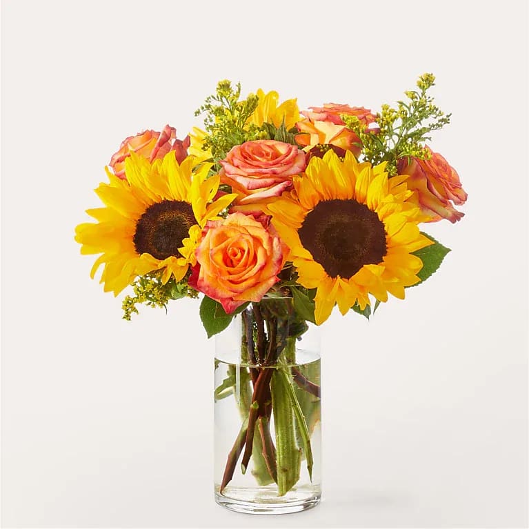 Sunflowers and orange-pink roses in a clear glass vase