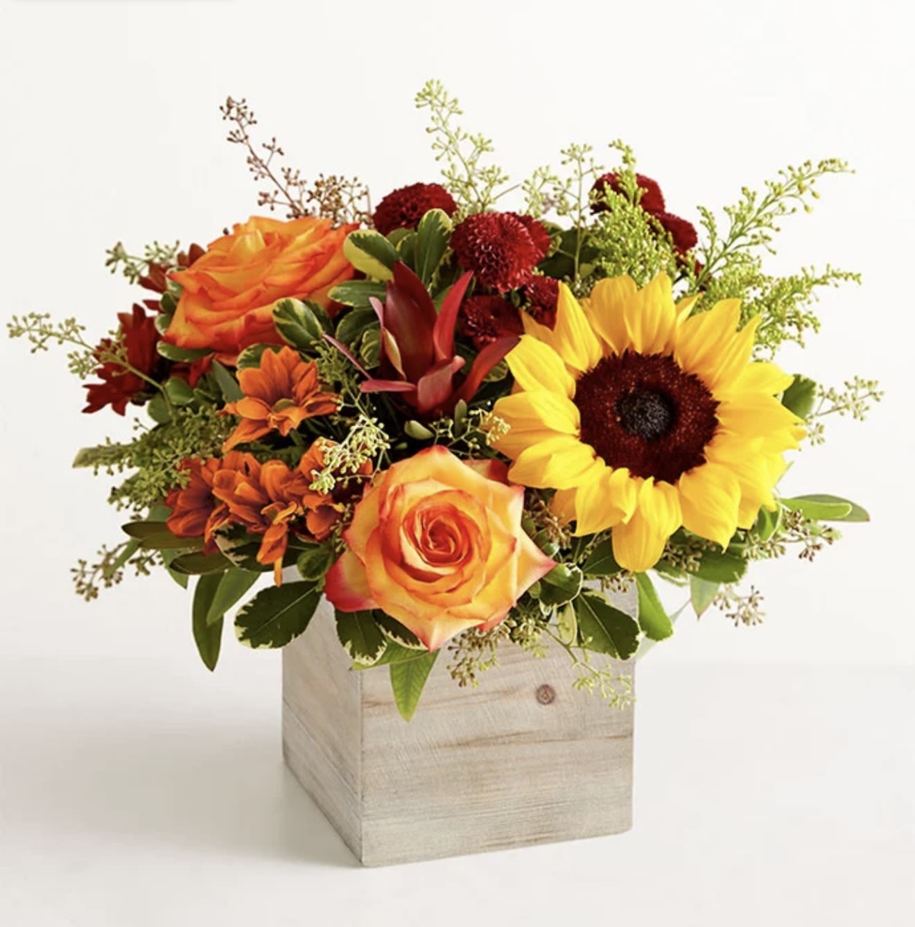 Harvest Glow Bouquet - The color and charm of an autumn country harvest inspired our farmhouse-style bouquet. A relaxed gathering of blooms in vibrant shades of red, orange, and yellow creates the perfect complement to our rustic, wooden cube, which adds coziness to any décor.